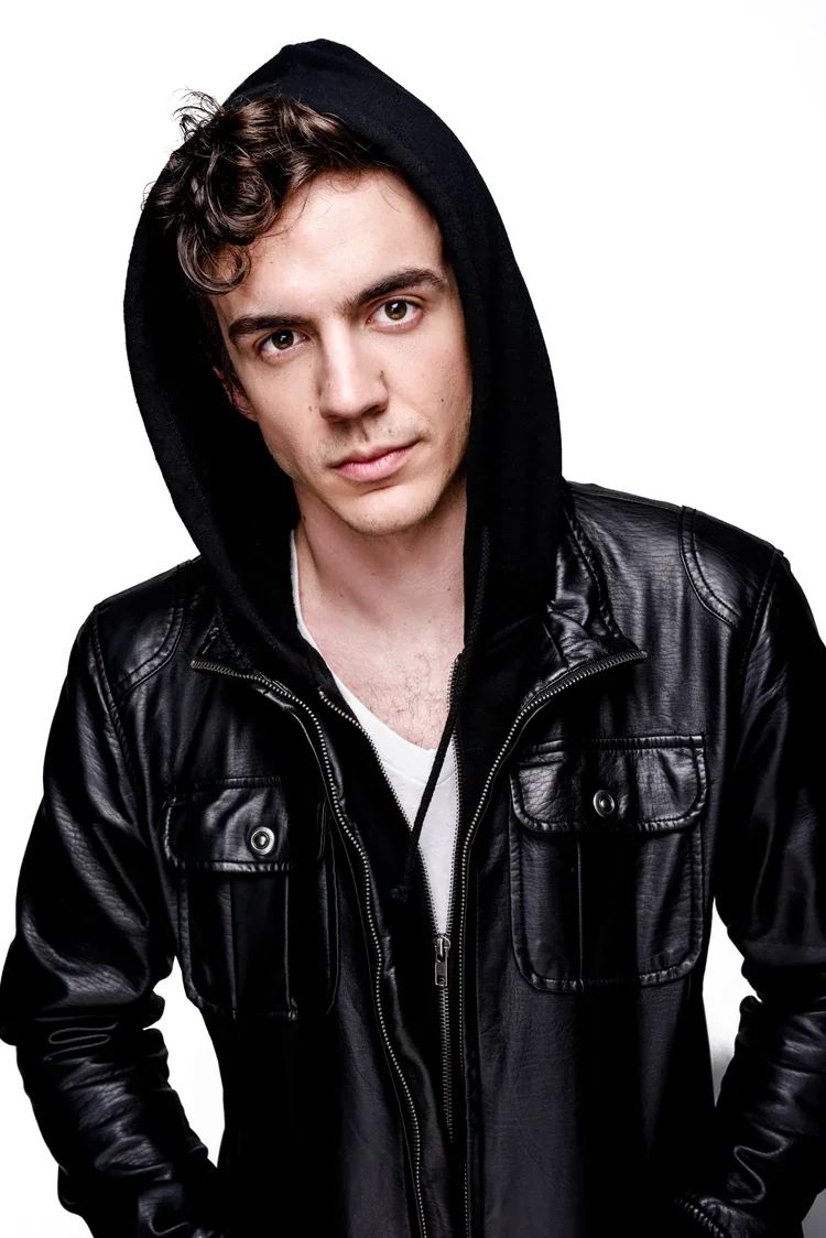 Young man wearing a black hoodie and leather jacket against a white background.