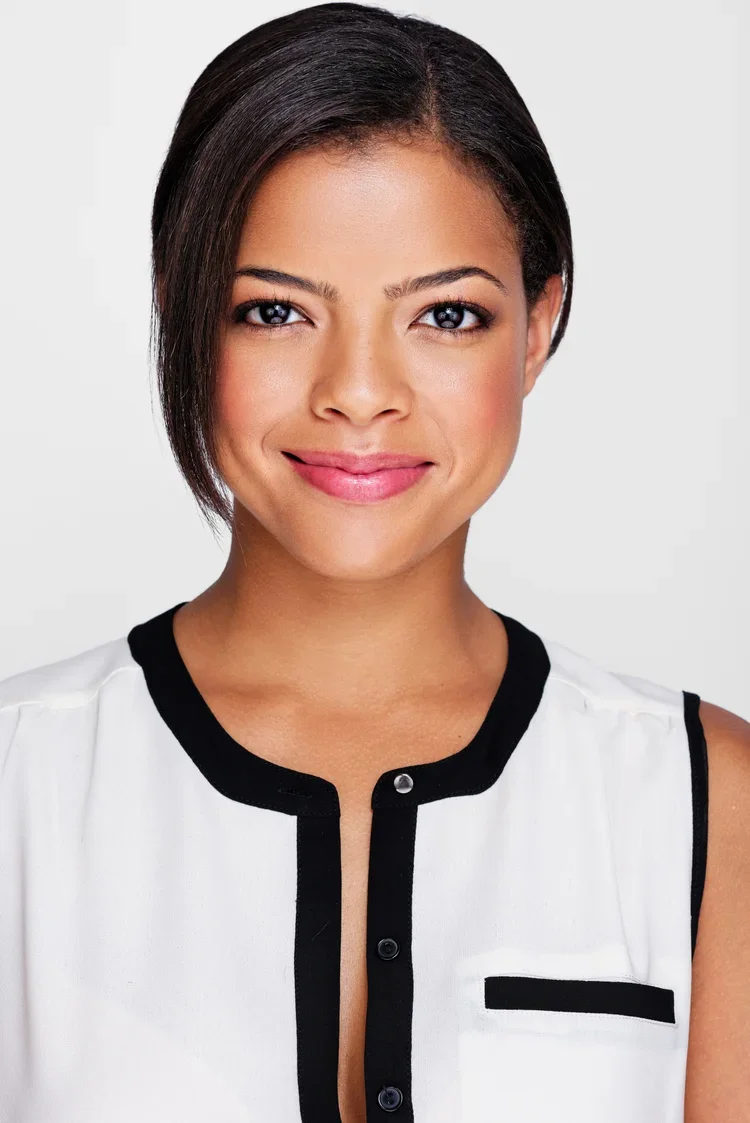A young woman with short, dark hair, smiling, wearing a white sleeveless top with black trim.