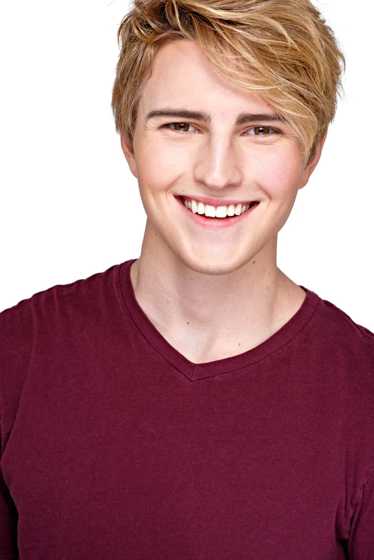 Young man with blond hair smiling, wearing a maroon T-shirt, against a white background.