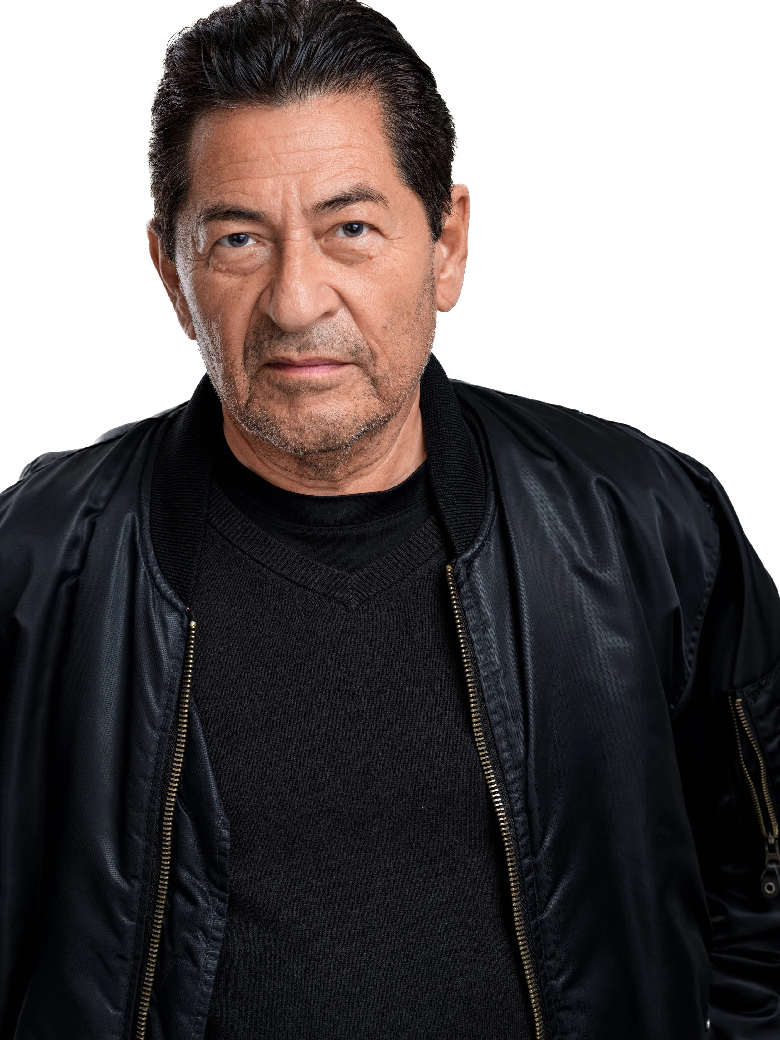 A middle-aged man with dark hair, some gray, wearing a black leather jacket over a black shirt, looking directly at the camera with a neutral expression.