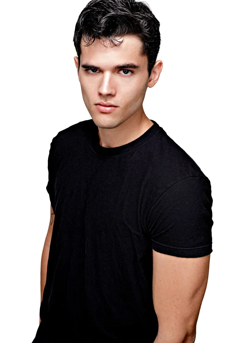 A young man with dark hair and light skin wearing a black t-shirt, looking directly at the camera against a plain white background.