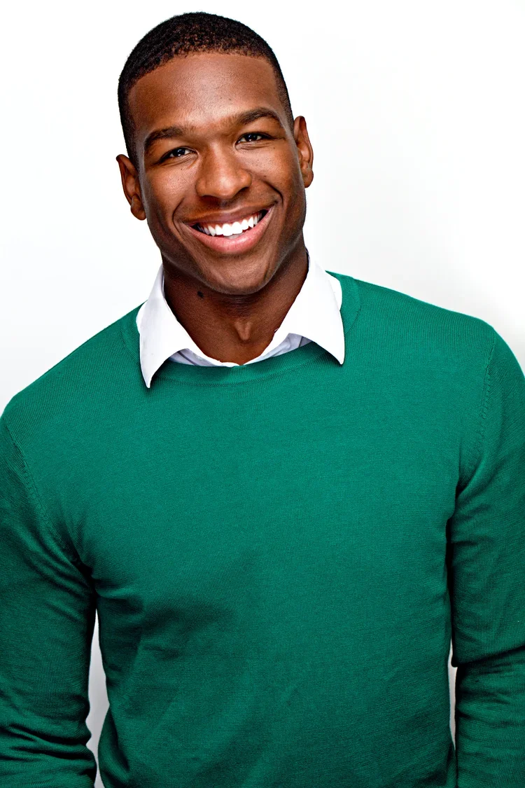 Smiling man in green sweater and white collared shirt against white background.