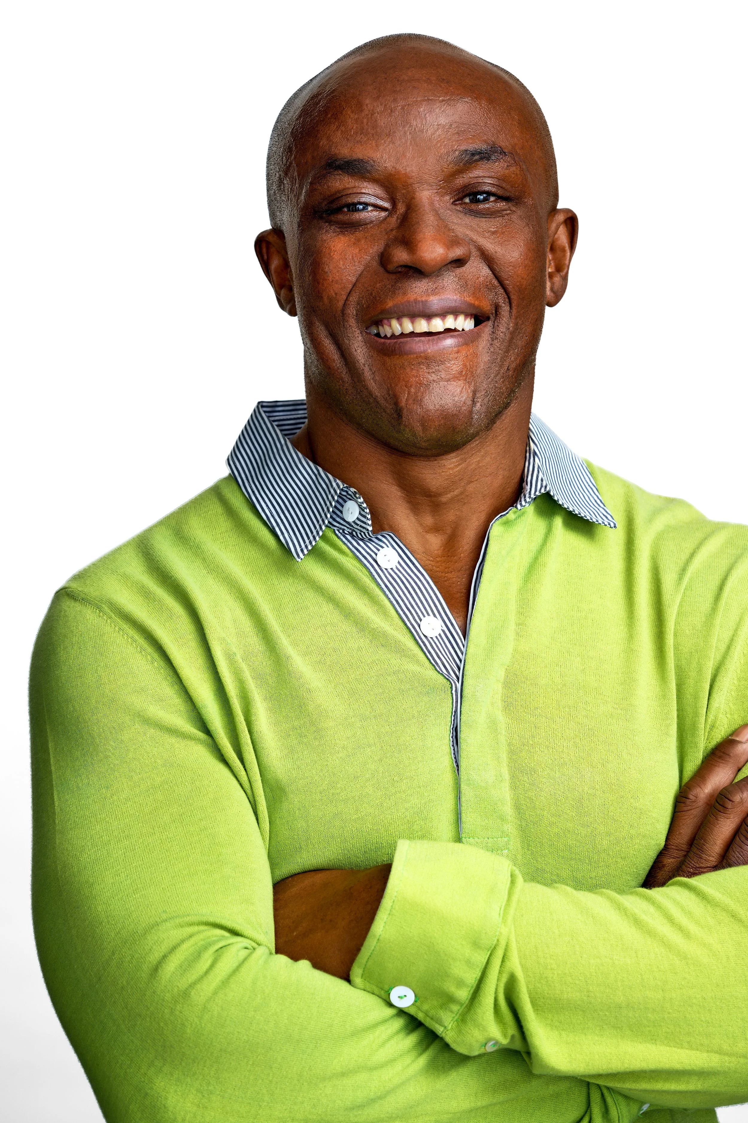 Close-up of a smiling African American man in a green sweater and a collared shirt, with arms crossed and a white background.