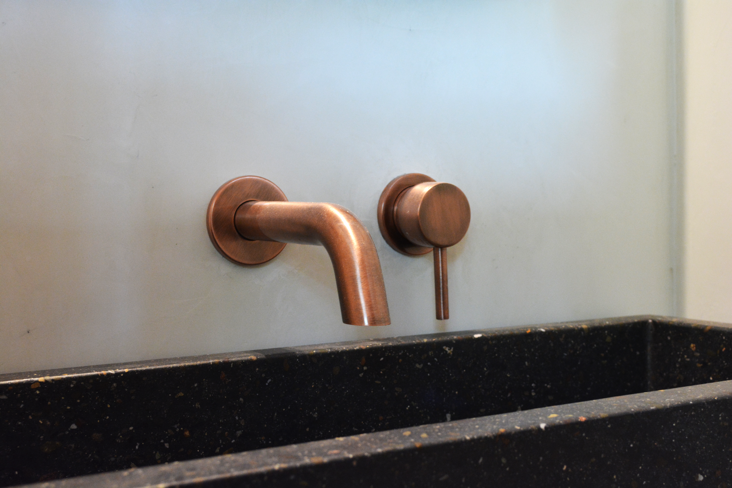 Bronze wall-mounted faucet above a black speckled sink in a bathroom or kitchen.