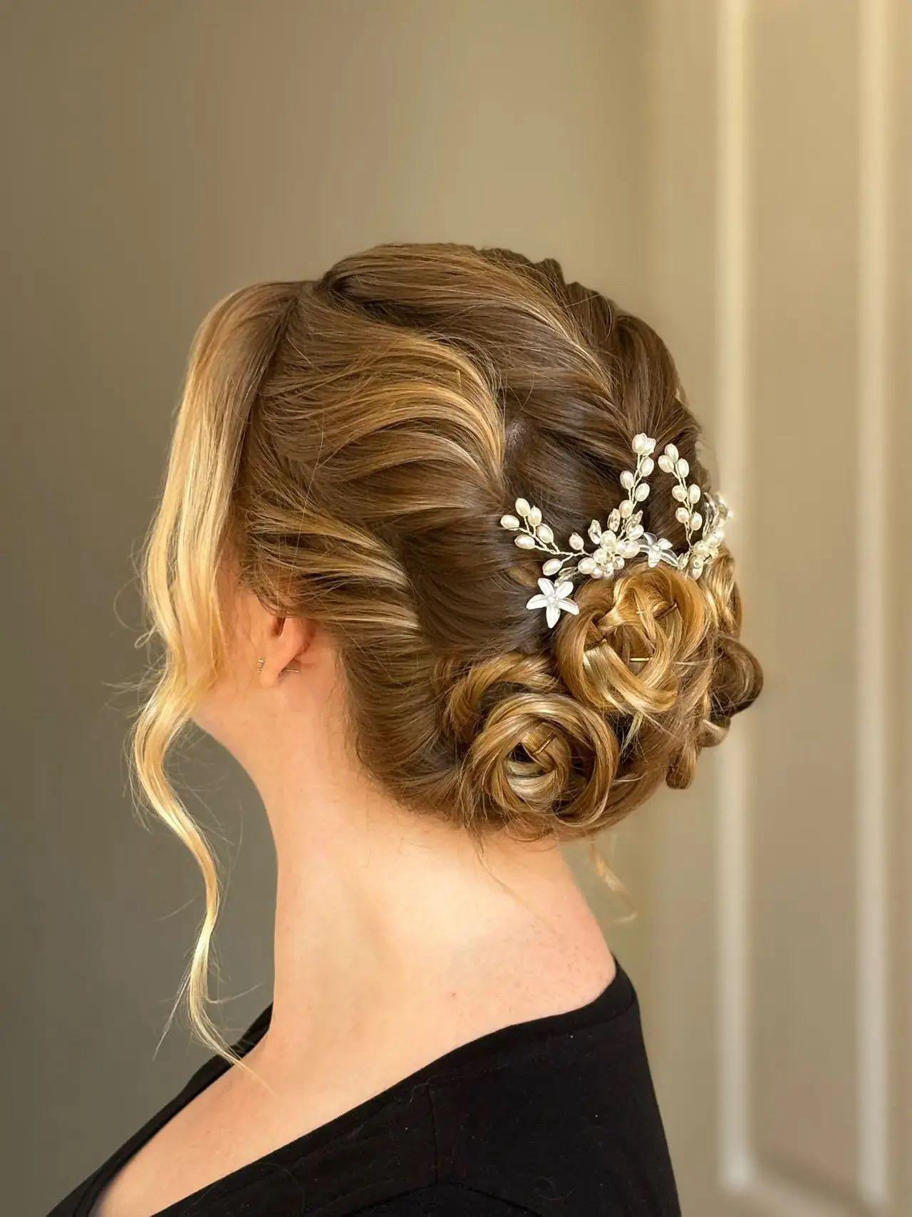 Elegant updo hairstyle with intricate braids and curls, adorned with a pearl and floral hair accessory.