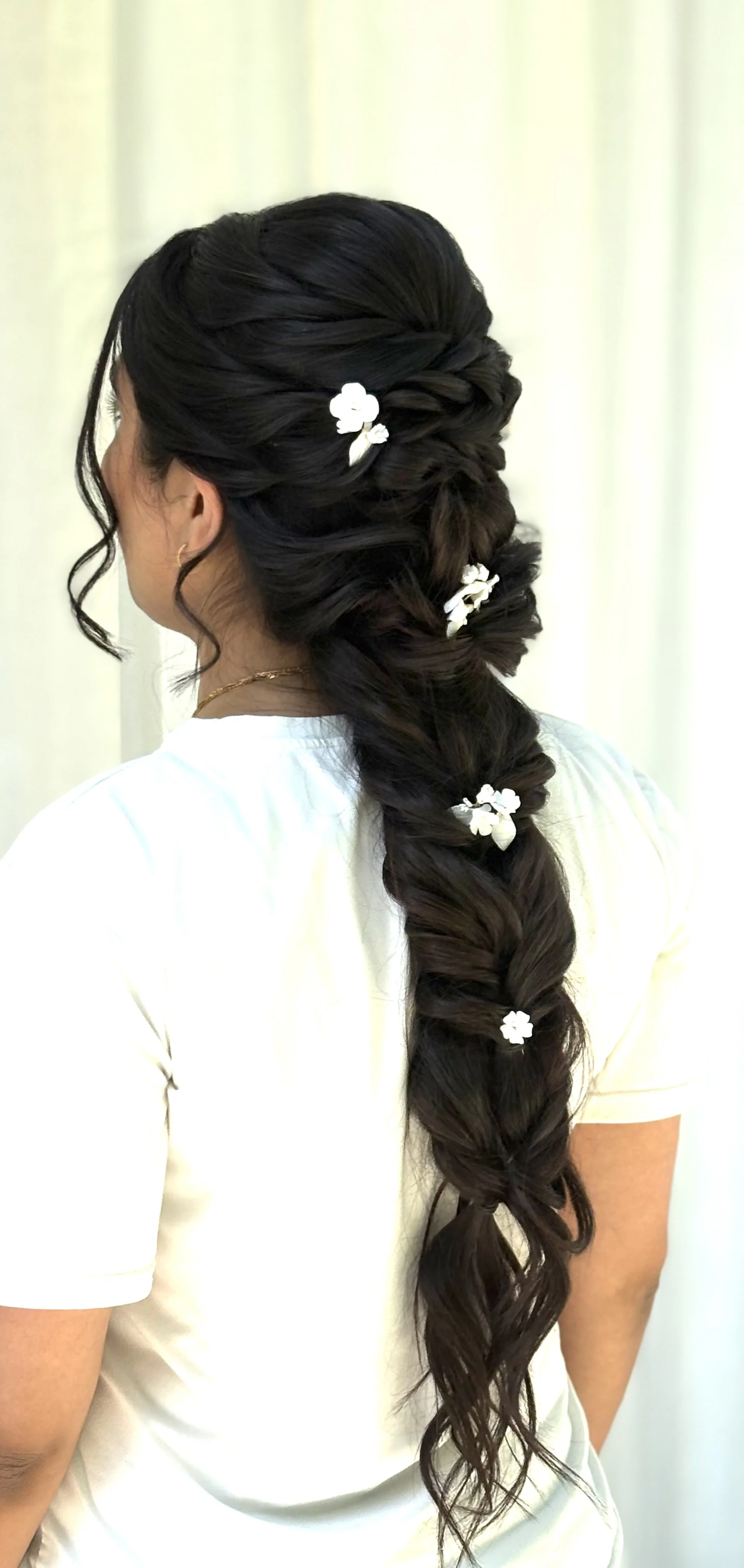 Close-up of a woman’s long, dark braided hairstyle decorated with white flower accessories.