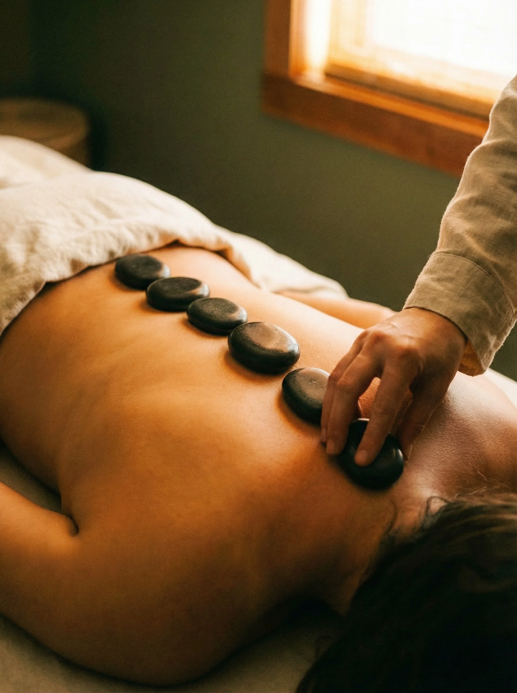 A person receiving hot stone massage therapy on their back in a spa or massage room.