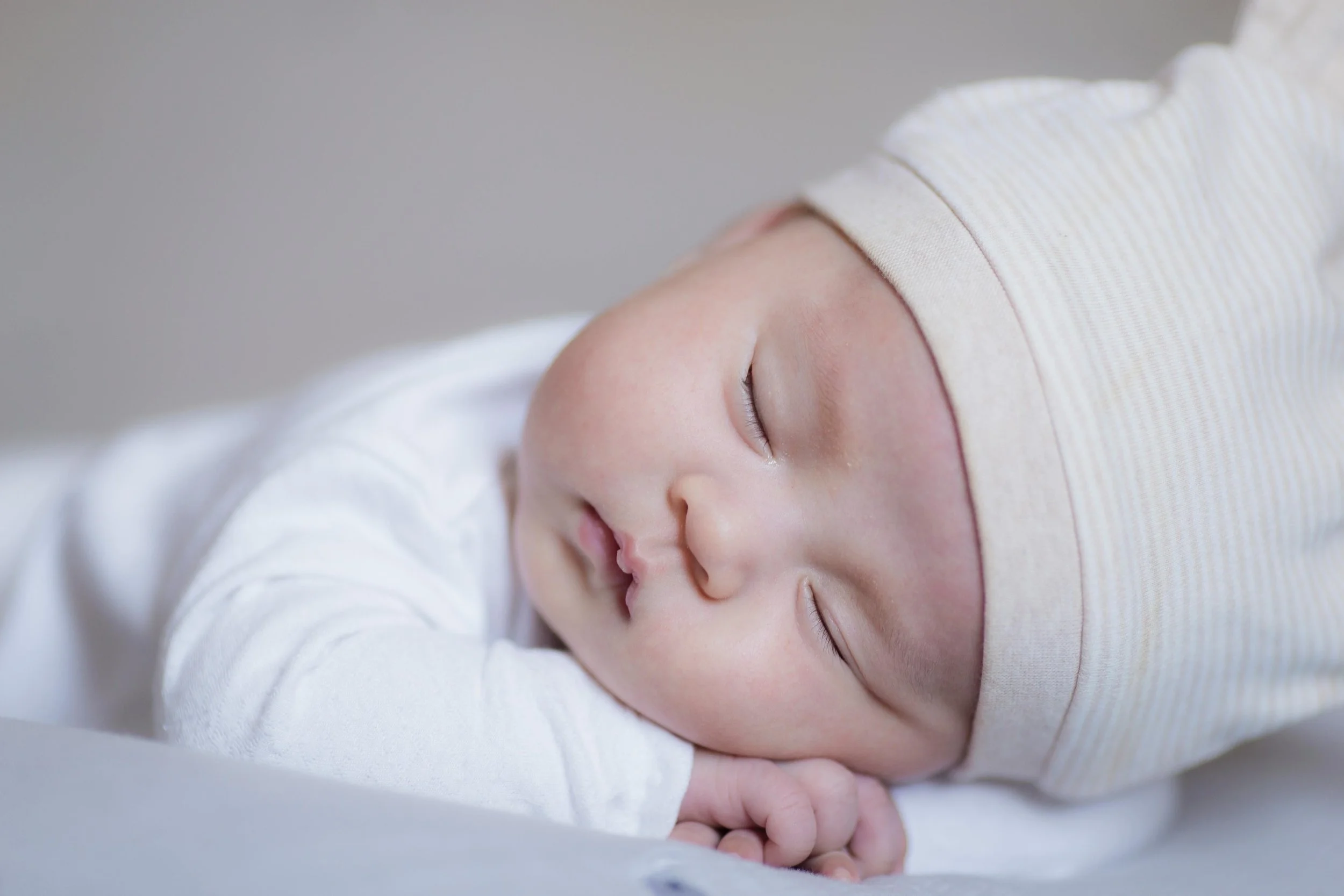 Close-up of a sleeping baby with a beige striped hat lying on a white surface.