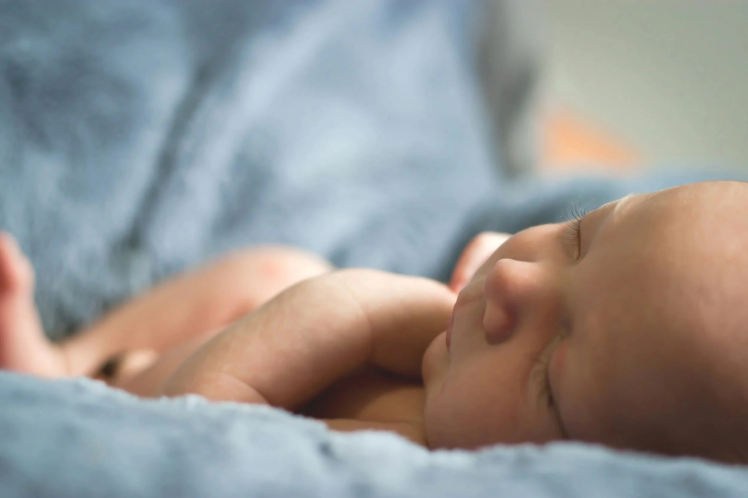 Close-up of a sleeping baby being held gently in an adult's arms, with soft lighting and a blurred background.