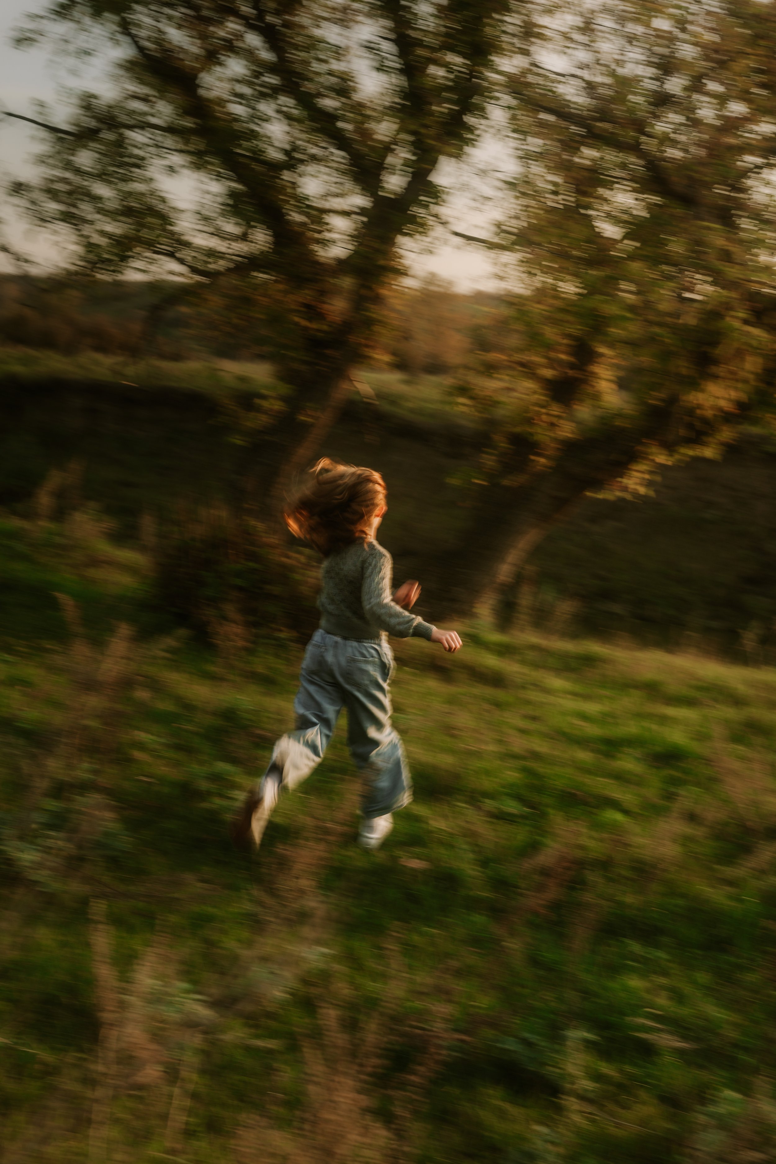 A child running outdoors in a grassy area with trees in the background during sunset.