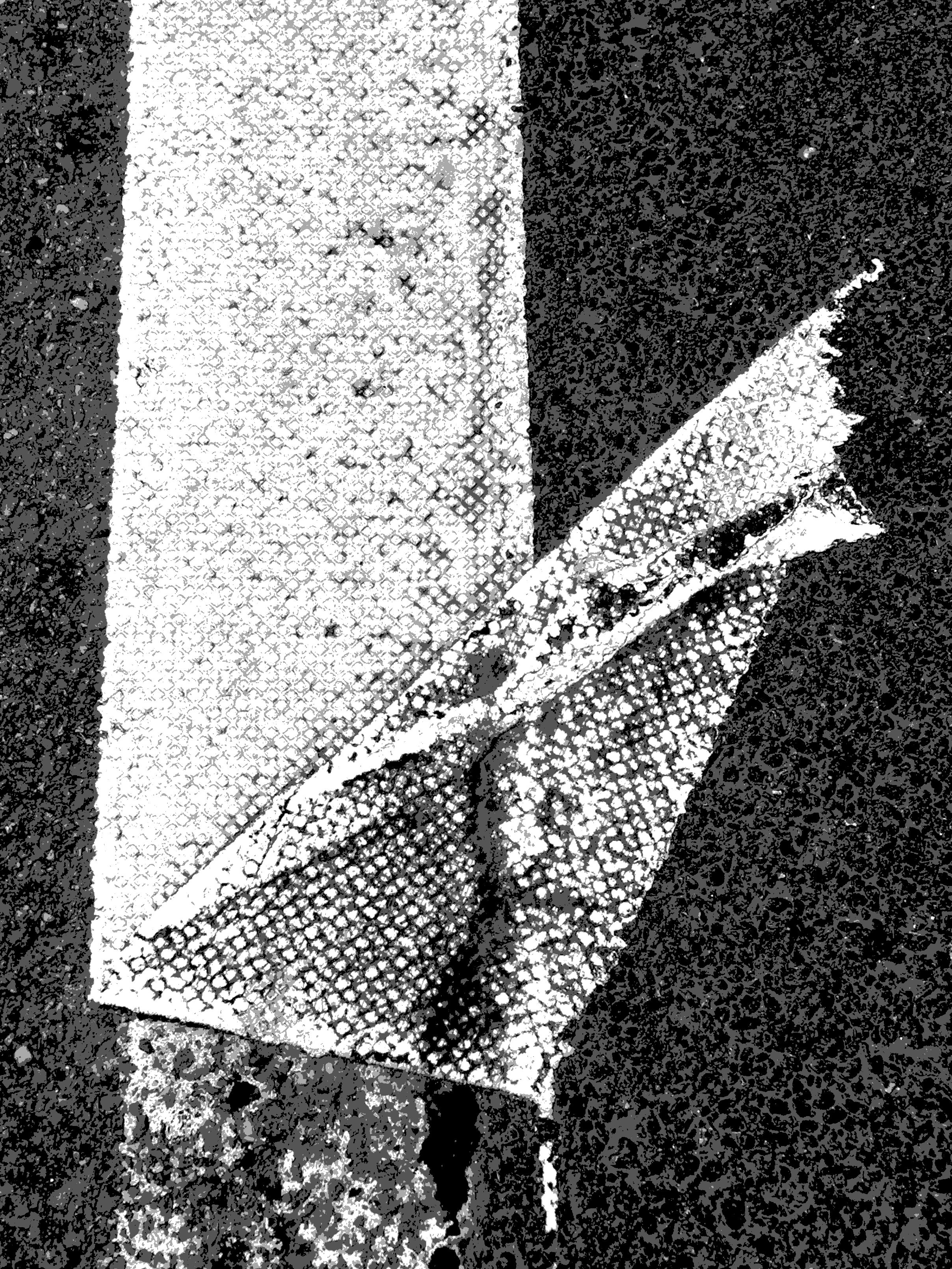 Close-up of a painted traffic lane marking, with torn and worn white paint on a dark asphalt surface.