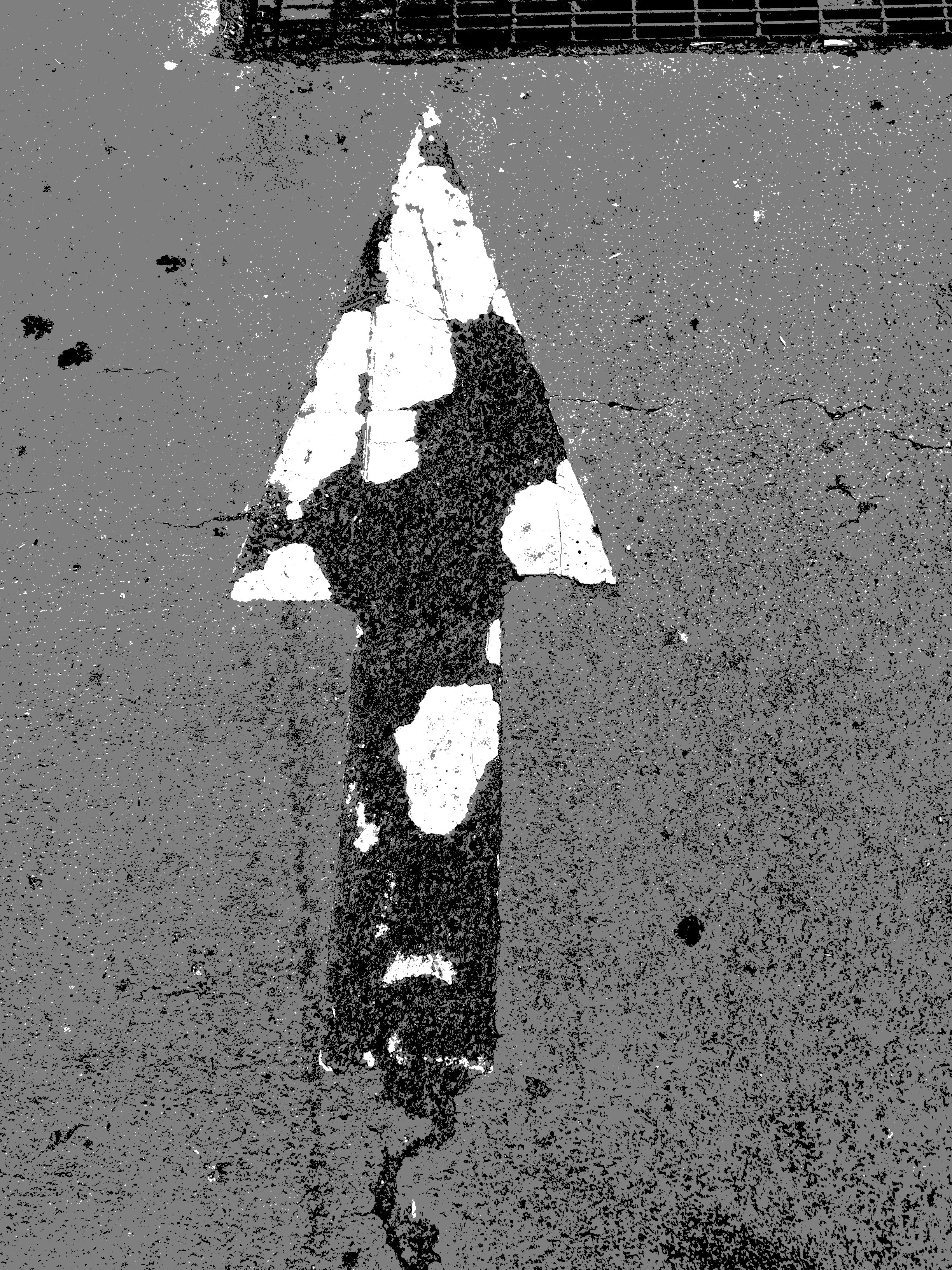 Black and white photograph of a pedestrian crosswalk on a cracked asphalt road, with a shadow or footstep crossing over the white lines.