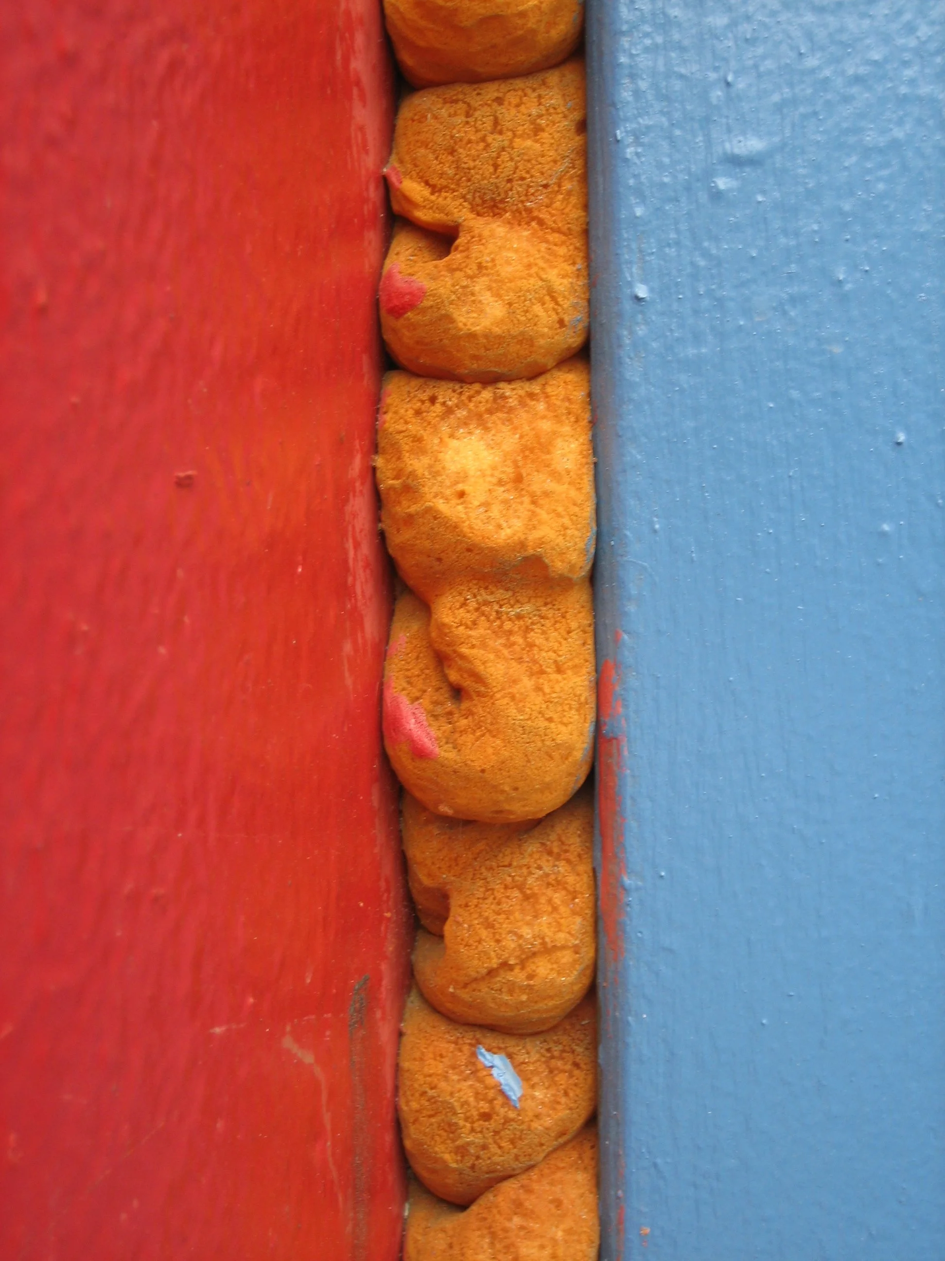 Colorful stones or rocks arranged between a red surface on the left and a blue surface on the right, seen from the side.