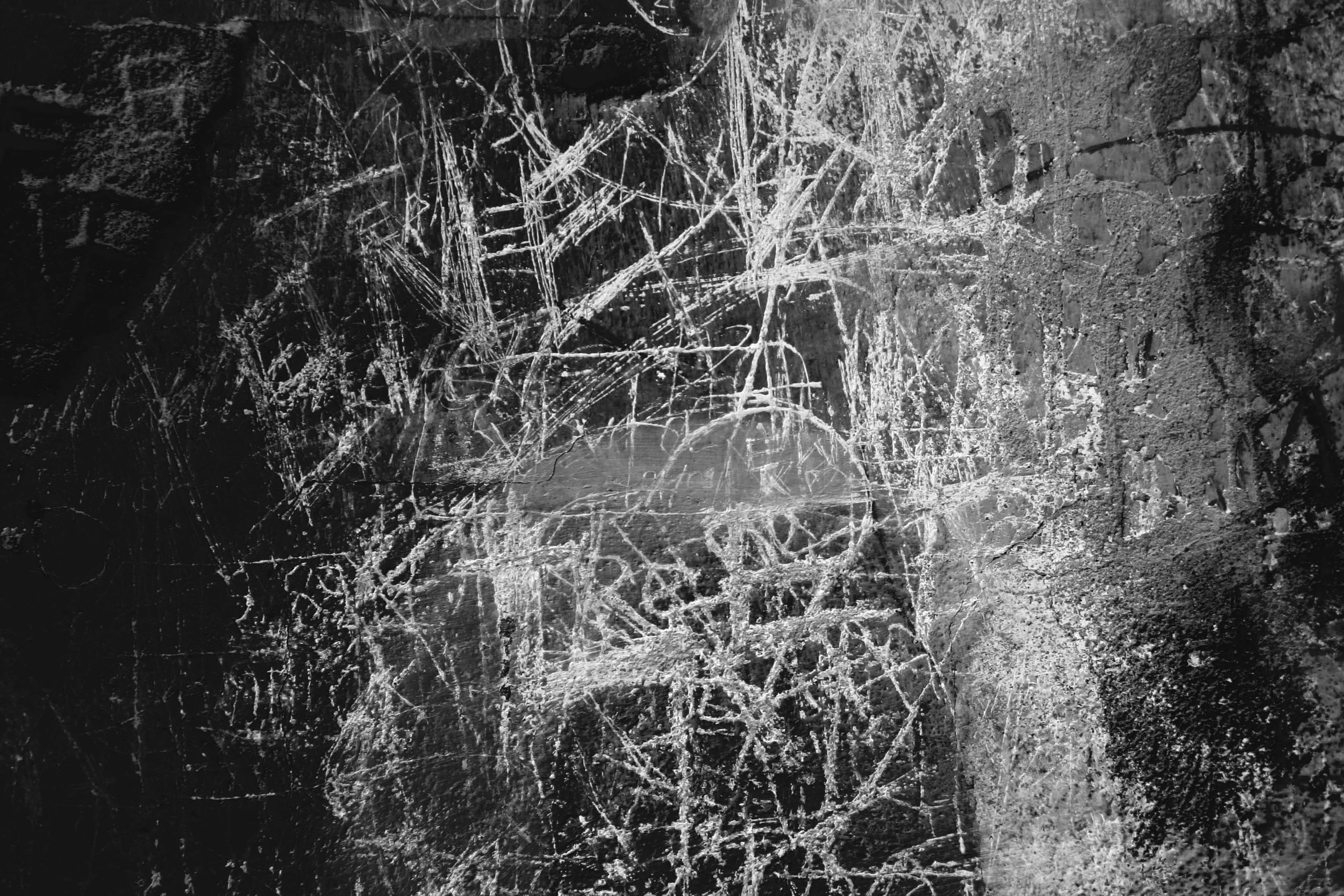 A black and white textured surface with a pattern of scratches and scribbles.