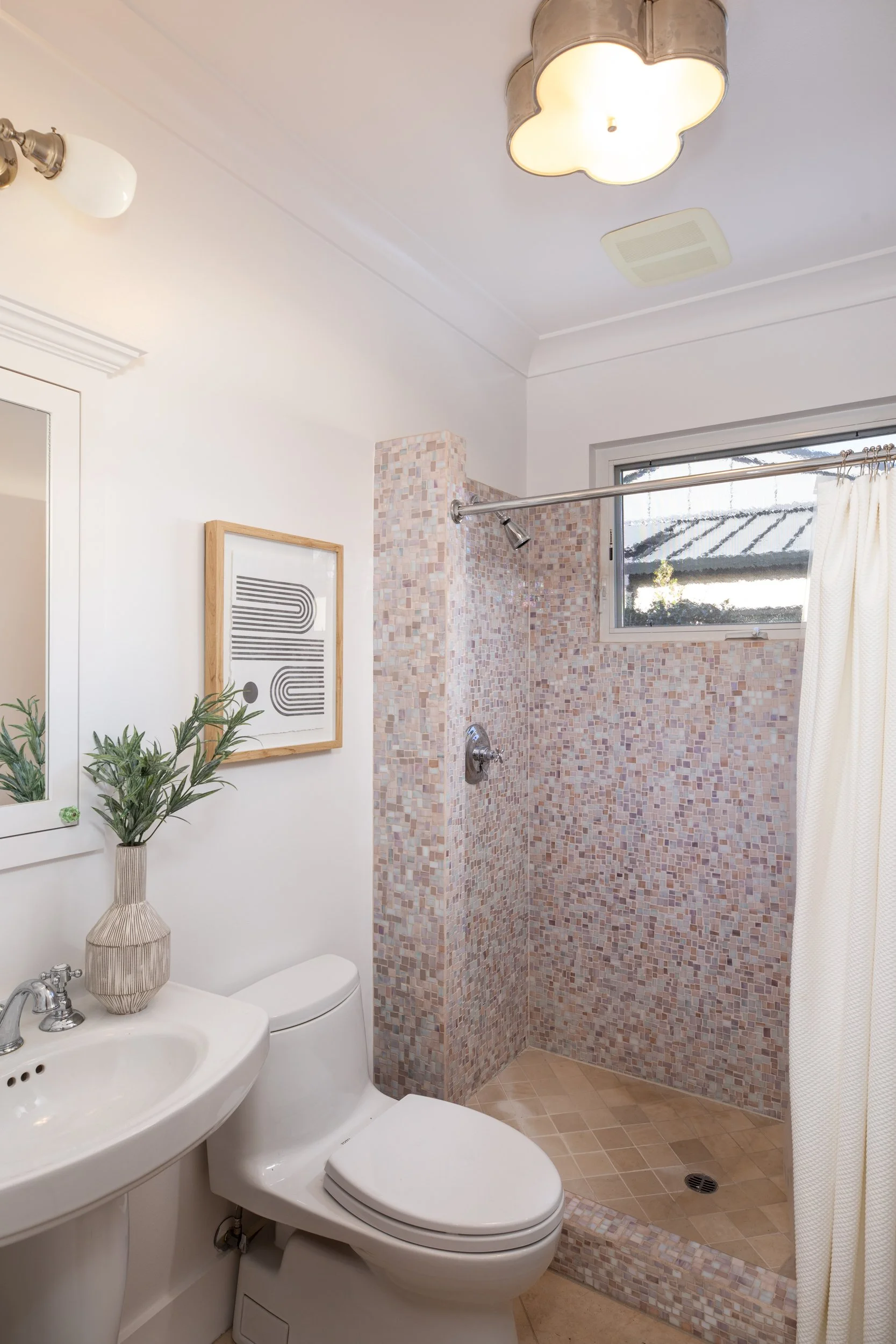 A bathroom with a white sink, a toilet, and a walk-in shower with mosaic tiles and a small window.