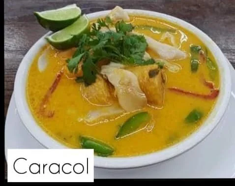 A bowl of yellow curry garnished with lime wedges, cilantro, and vegetable slices, labeled 'Caracol.'