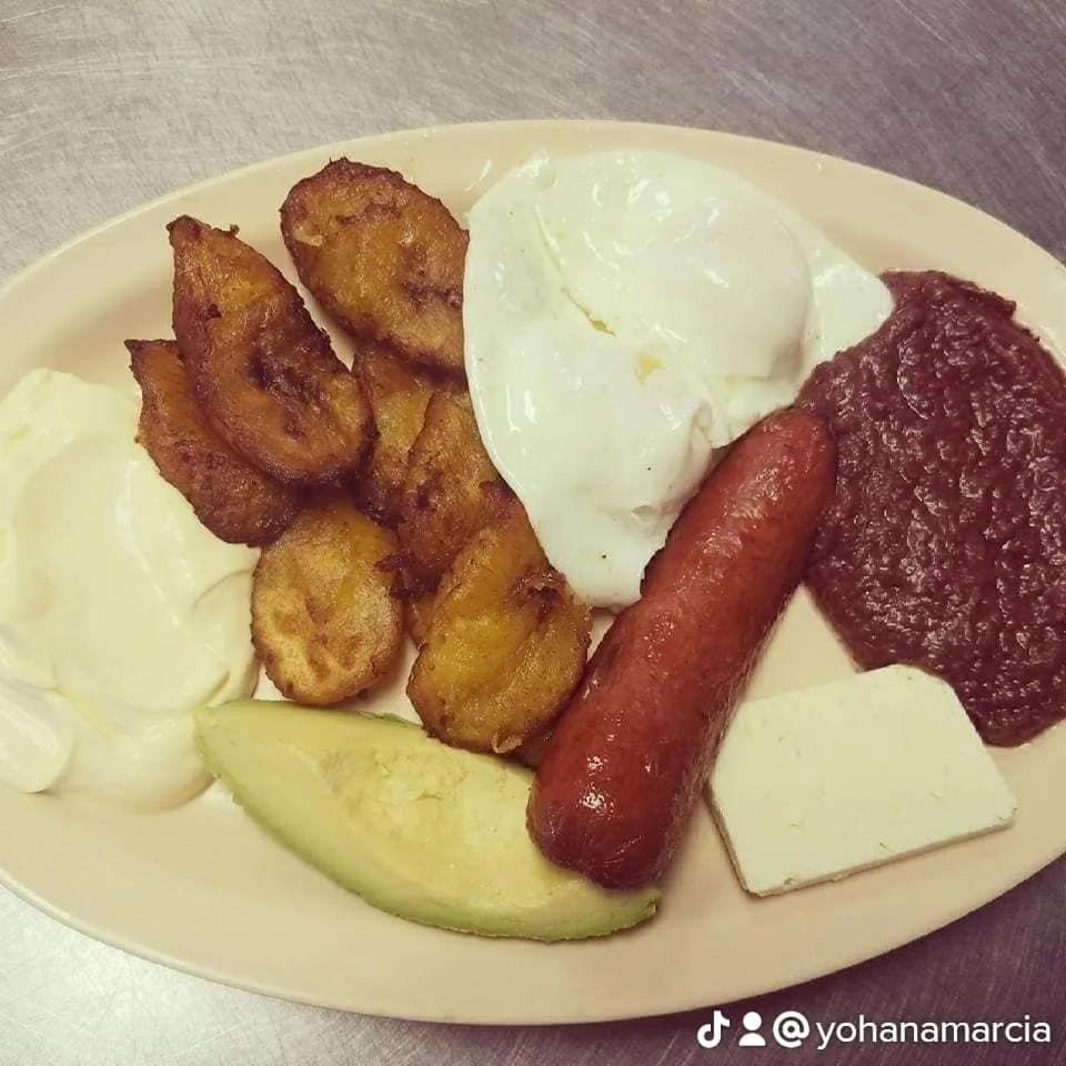 A plate with fried plantains, a poached egg, a sausage, refried beans, a slice of avocado, and a piece of queso blanco.