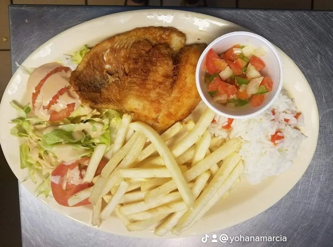 Fried fish fillet with French fries, a side of salad, chopped tomatoes and onions in a small cup, and a serving of white rice with diced vegetables.