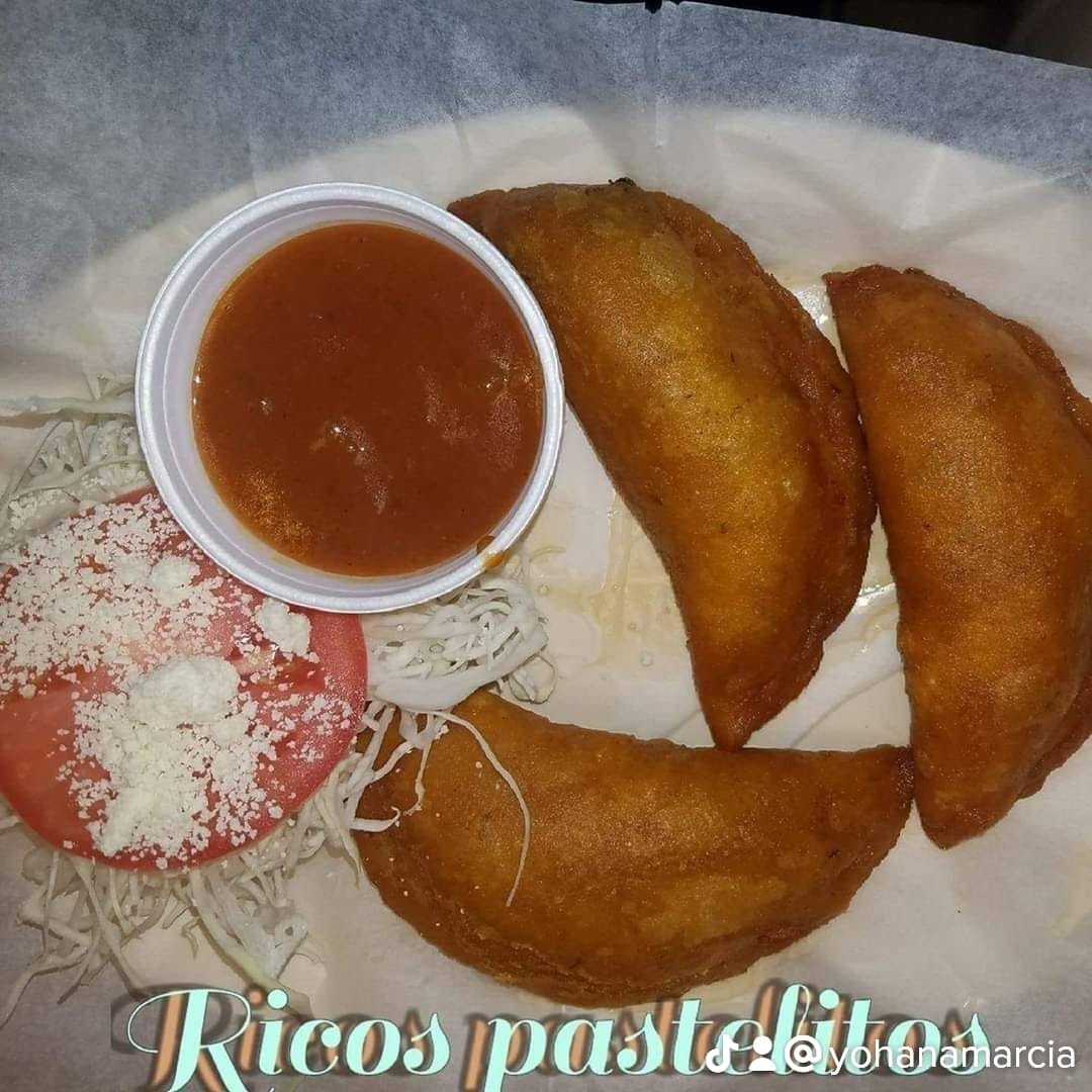 Three fried empanadas with a side of tomato, grated cheese, shredded lettuce, and a small cup of red sauce.