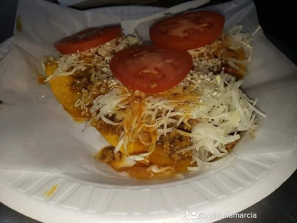 Close-up of a taco with ground beef, shredded lettuce, sliced tomato, and shredded cheese on a paper plate.