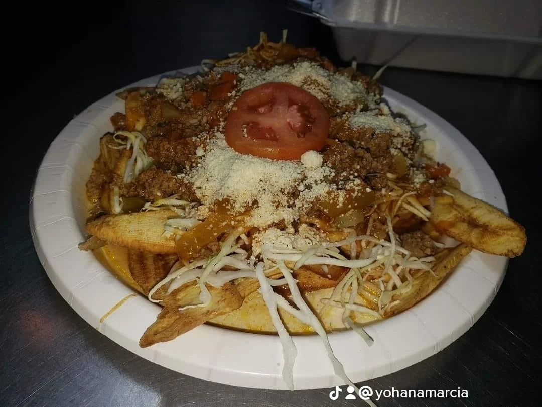 Plate of loaded nachos with fries, ground beef, shredded cheese, shredded lettuce, sliced tomato, sour cream, and hot sauce.