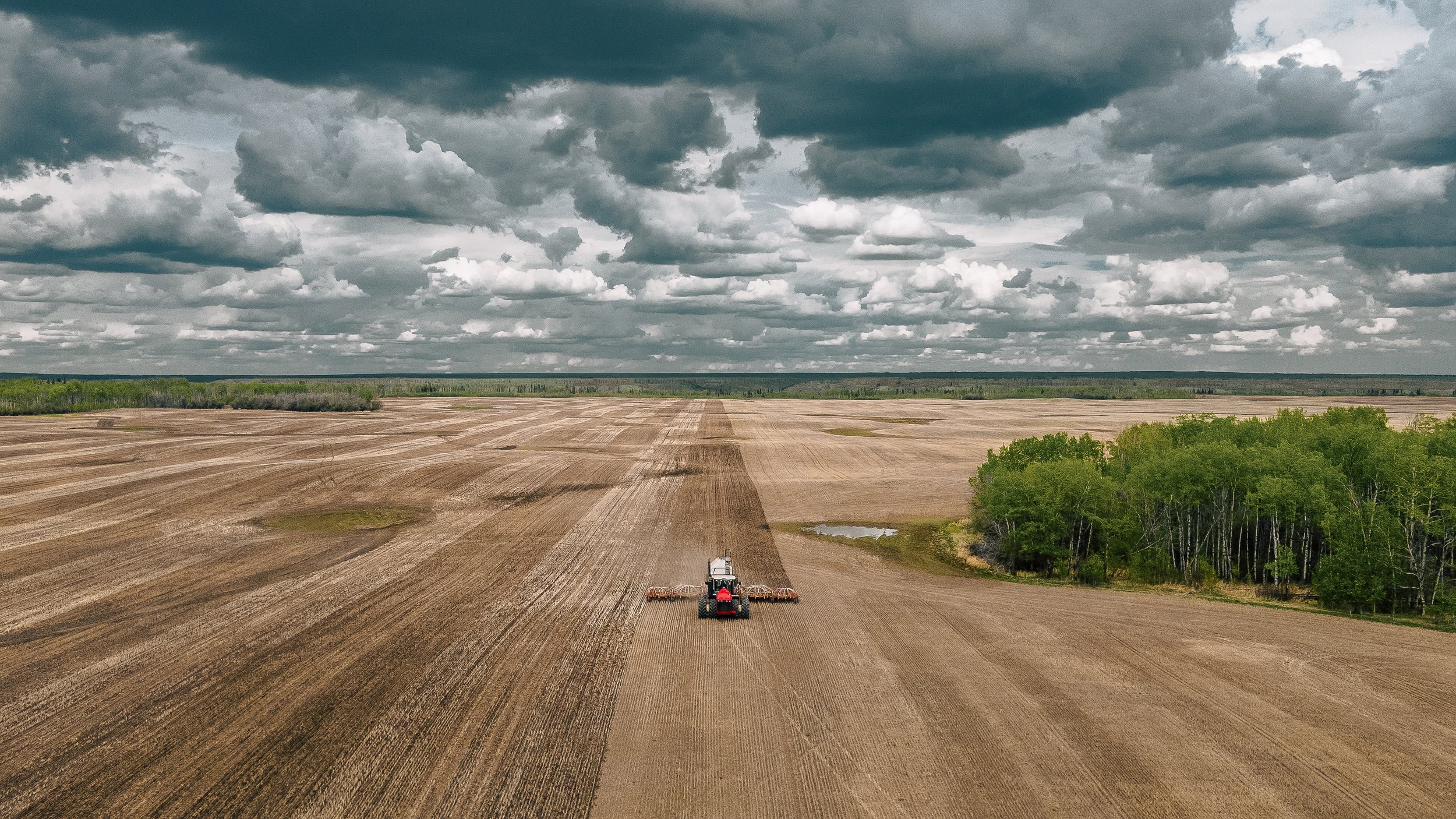 A tractor working on a large open farmland field under a cloudy sky.