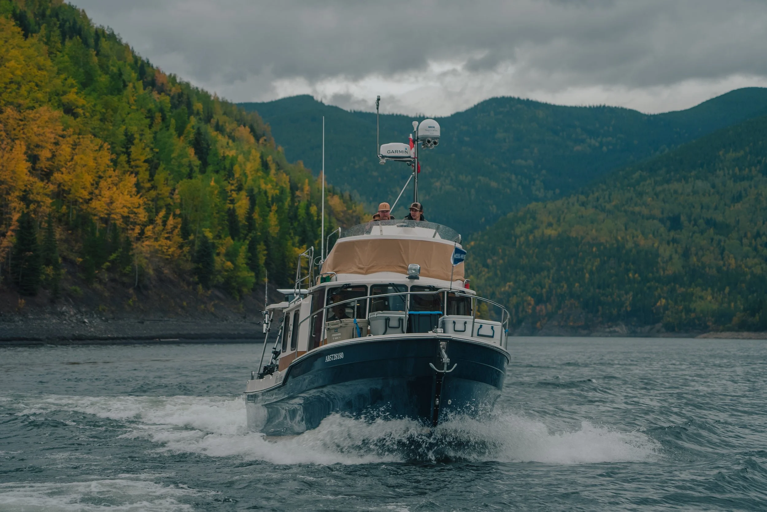A boat cruising on a lake with mountainous terrain and colorful autumn trees in the background.