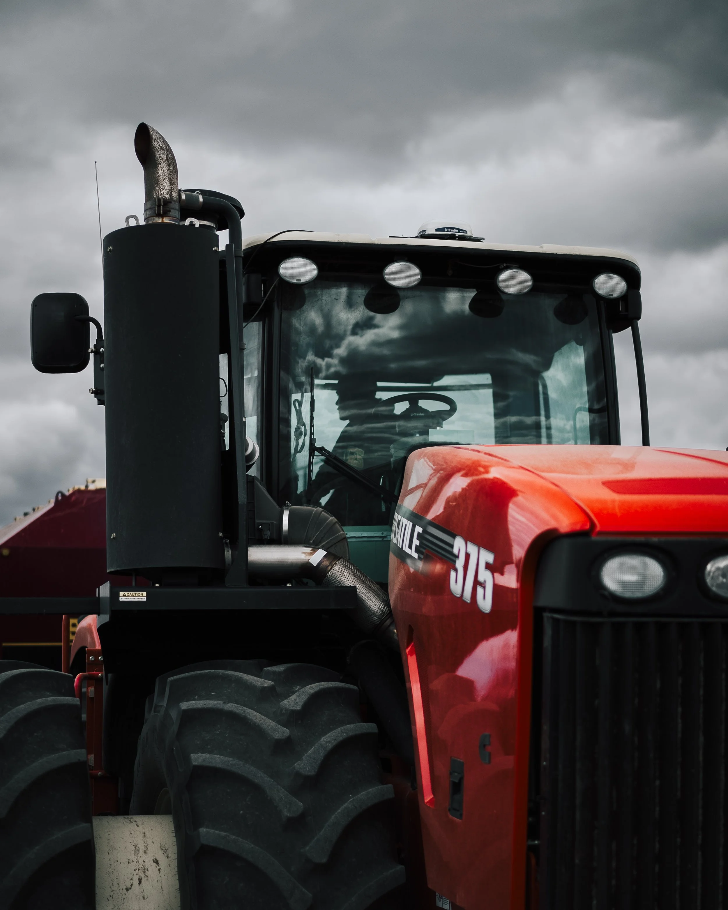 A red tractor with a black exhaust pipe and a large front tire, parked under a cloudy sky.
