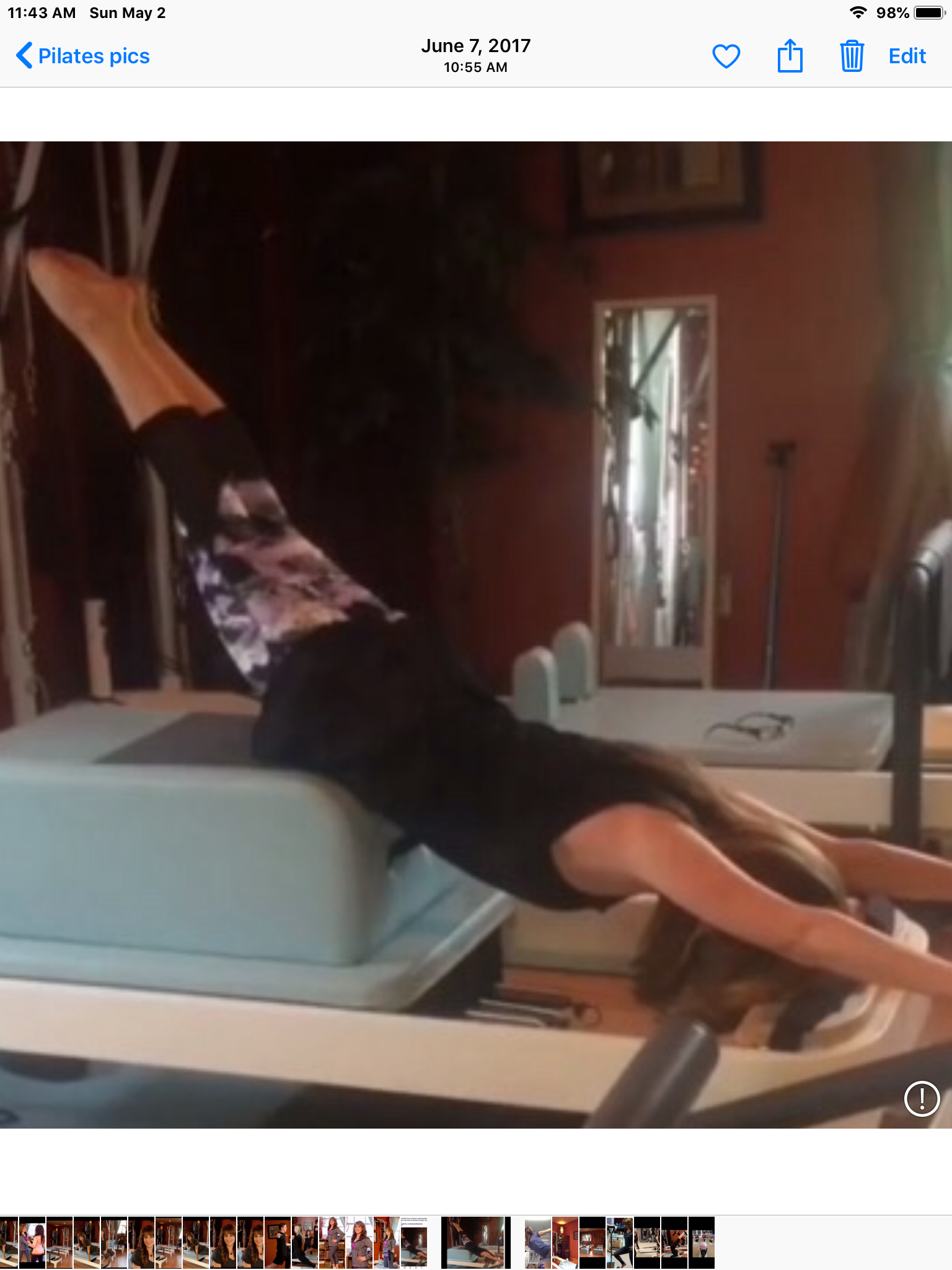 A woman lying face down on an exercise table with her legs raised and extended upward, in a Pilates or fitness studio.