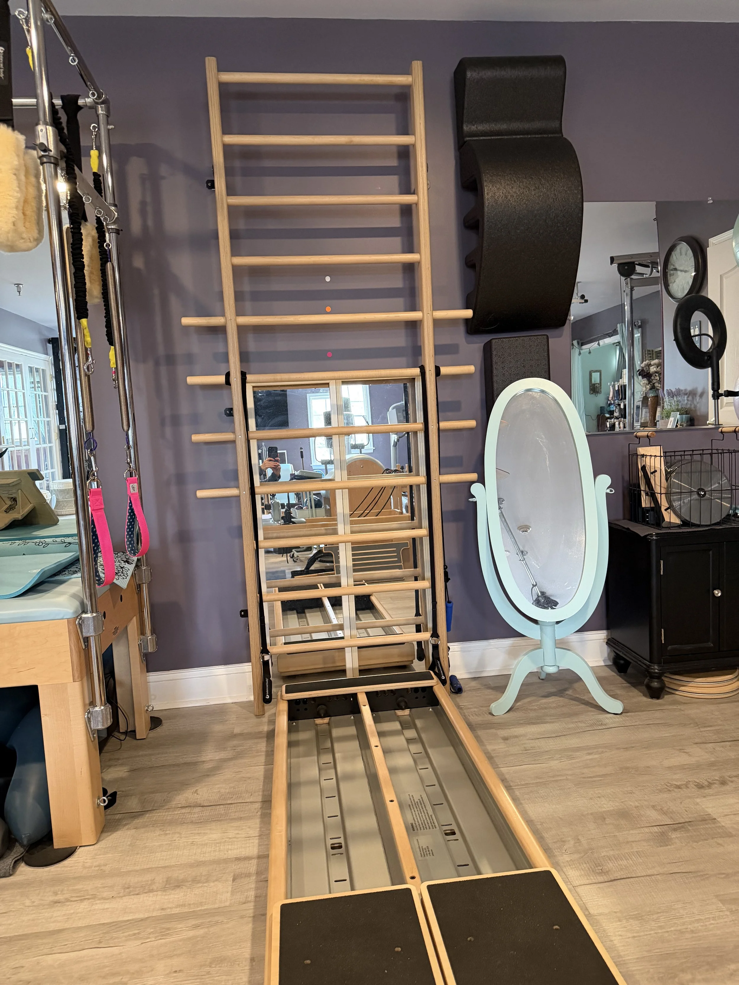 Indoor gym equipment including a wooden wall ladder, a mirror, and various fitness accessories.