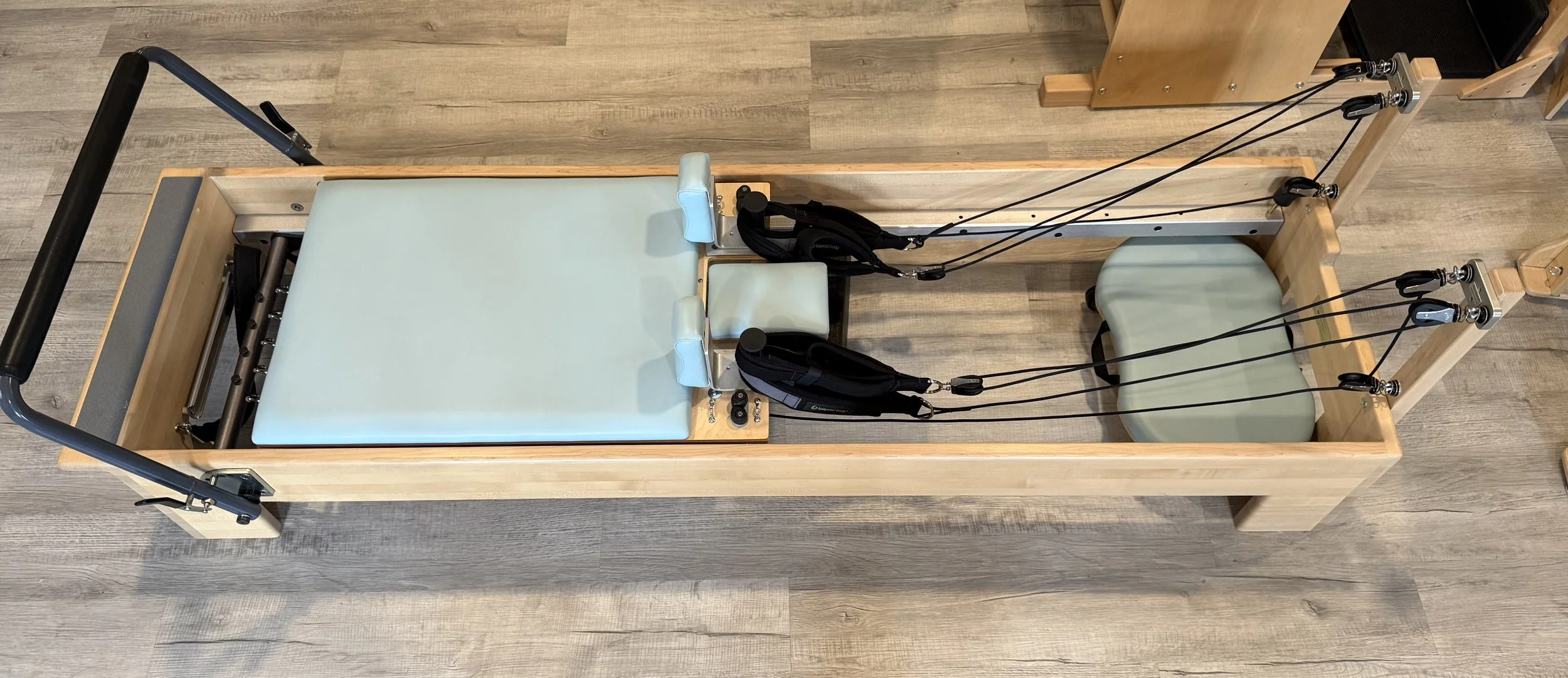 Rehabilitative reformer with pulleys, straps, padded and foam cushions, and a wooden frame, used for physical therapy exercises.