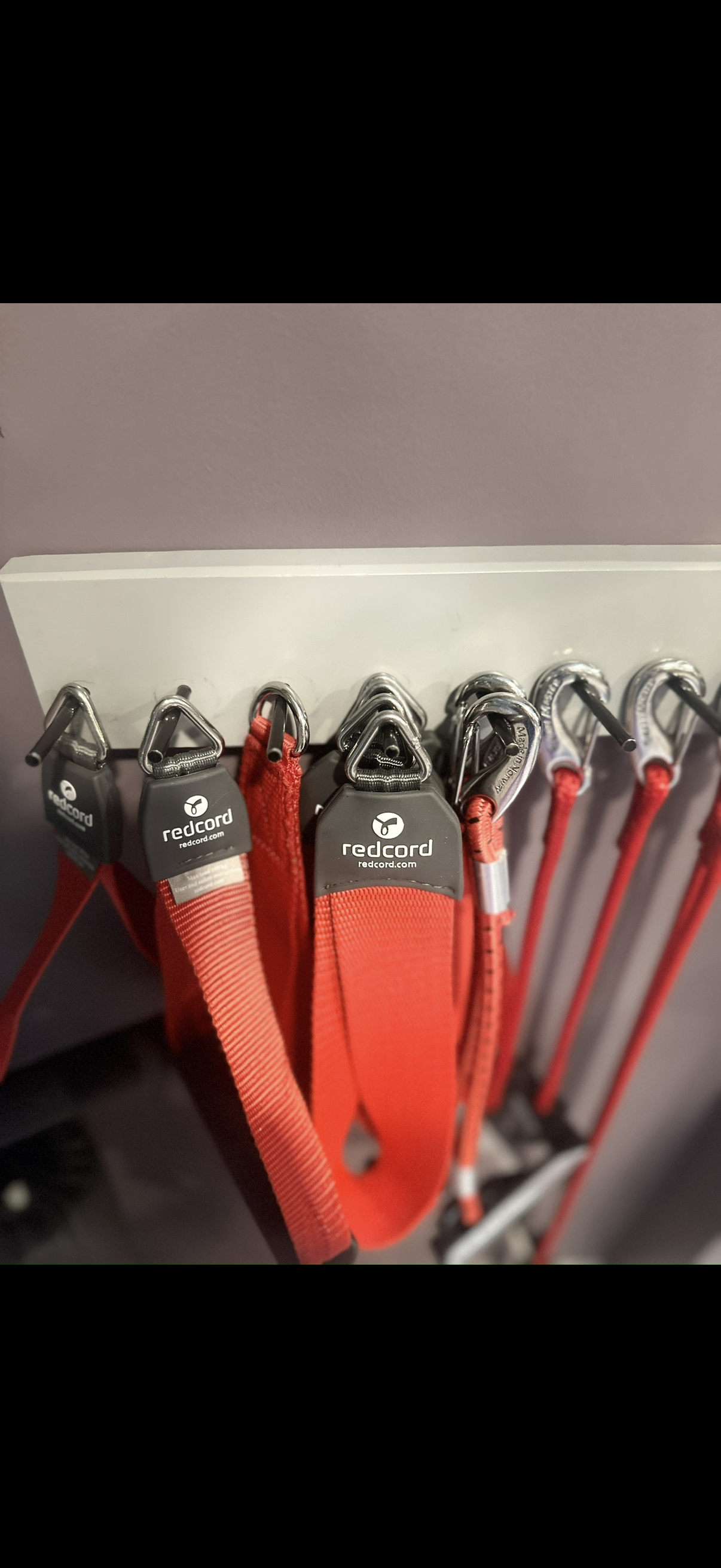 Red climbing harnesses hanging on hooks on a white accessory board, with carabiners attached.