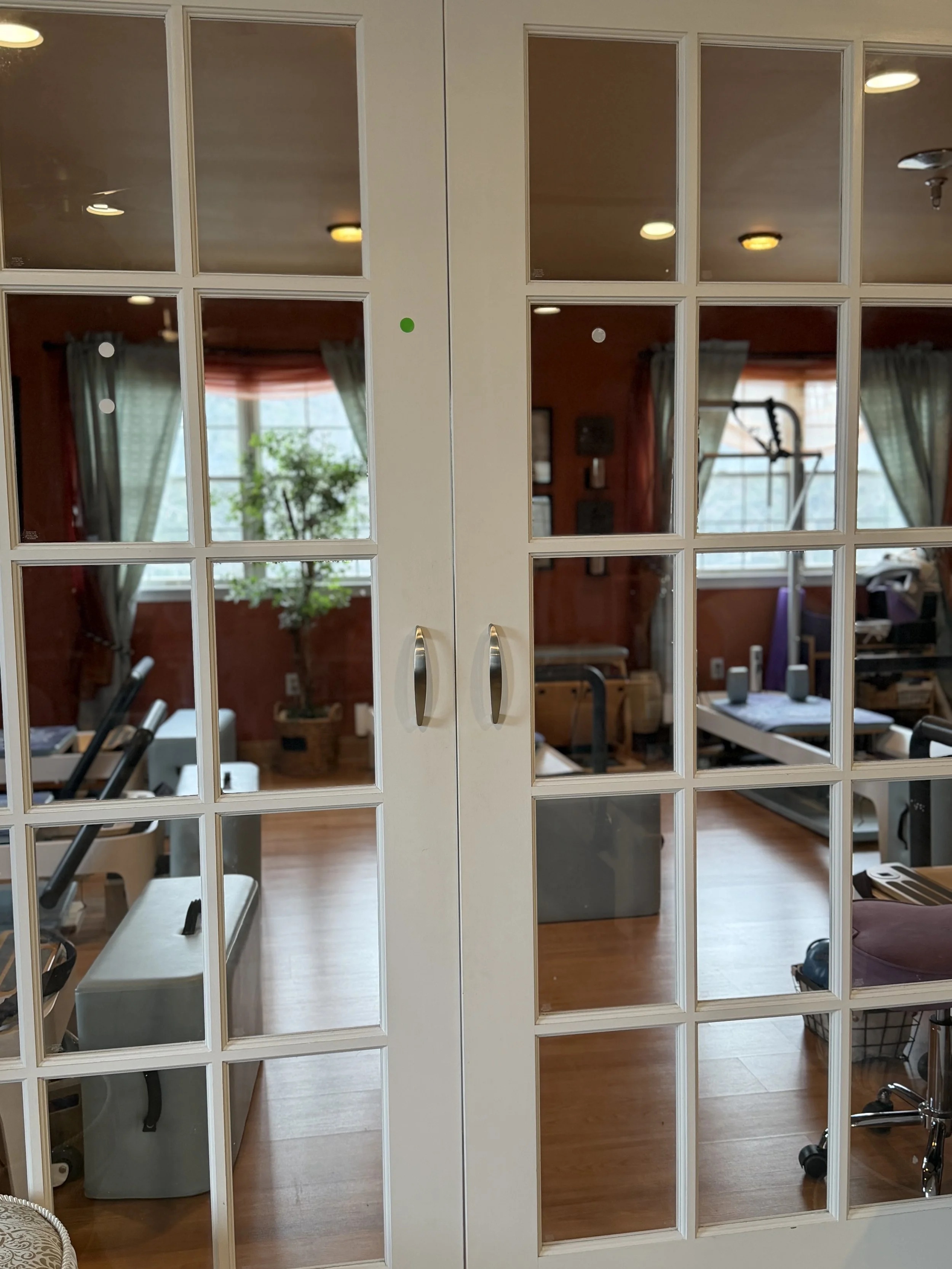 View through glass-paneled doors into a room with exercise equipment, a potted plant, and a large window with curtains.