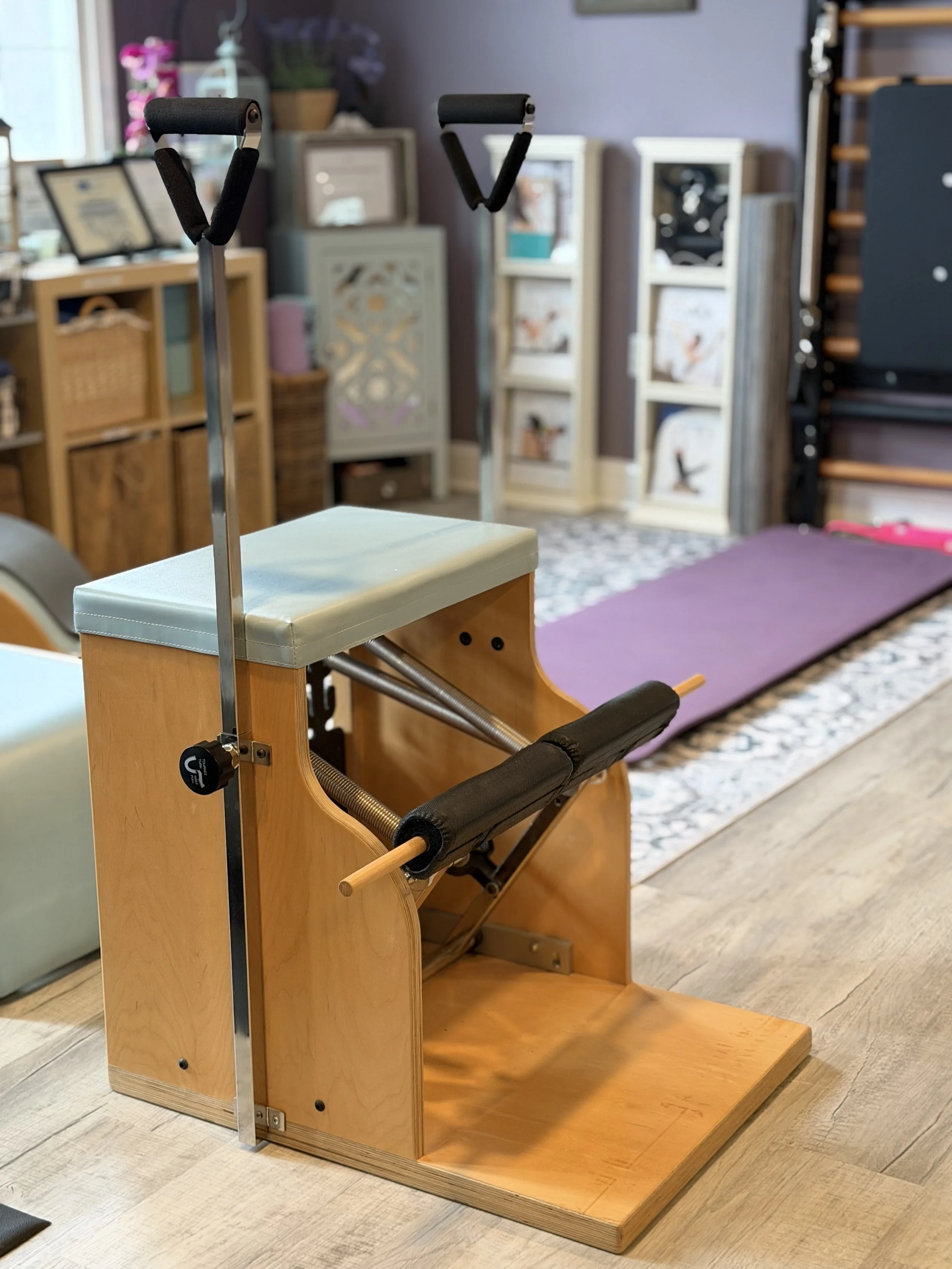Pilates reformer machine with wooden frame, padded platform, and resistance springs, located in a fitness studio with purple and beige decor.