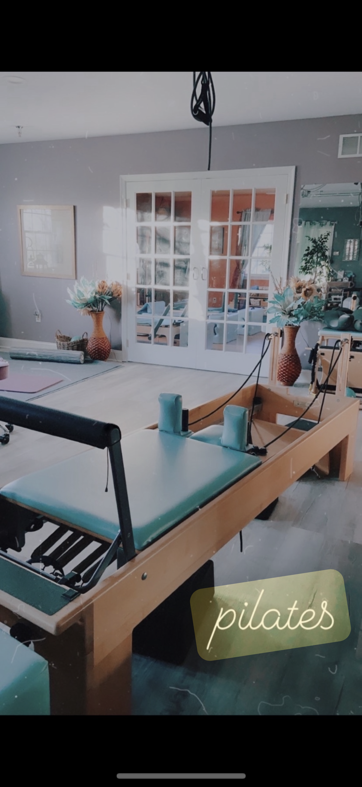 Indoor Pilates studio with a reformer machine, floral vases, and sliding glass doors leading to a bright room