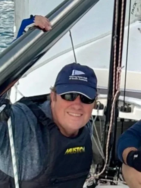 A man wearing sunglasses, a baseball cap, and a navy shirt, smiling on a boat.