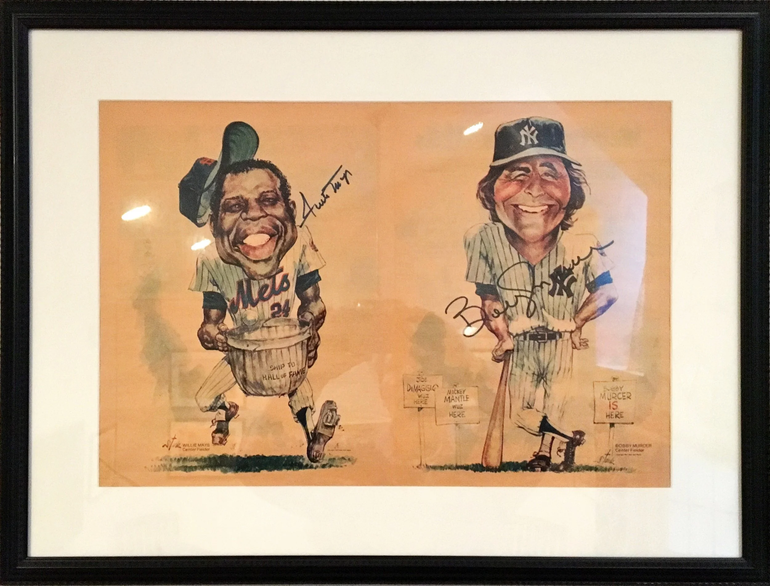 A framed caricature illustration of two baseball players in uniform, with signatures and name tags. The player on the left has dark skin, curly hair, and is wearing a cap and jersey with the word 'Mets.' The player on the right has lighter skin, long hair, and is wearing a cap with the New York Yankees logo and a striped uniform. The background is light orange, and the illustration is signed and labeled with names below each figure.