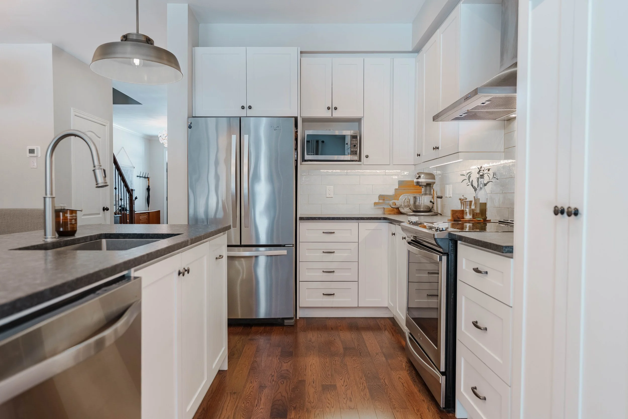 Modern kitchen with white cabinetry, stainless steel appliances, wooden flooring, and a gray countertop.