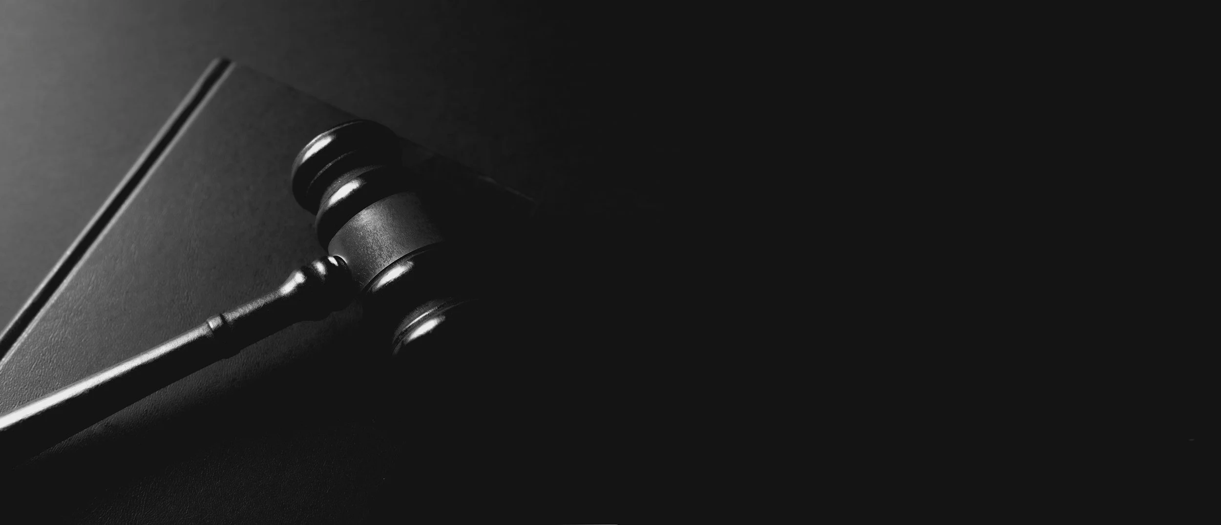 Black gavel resting on a black surface with a dark background, symbolizing law or justice.