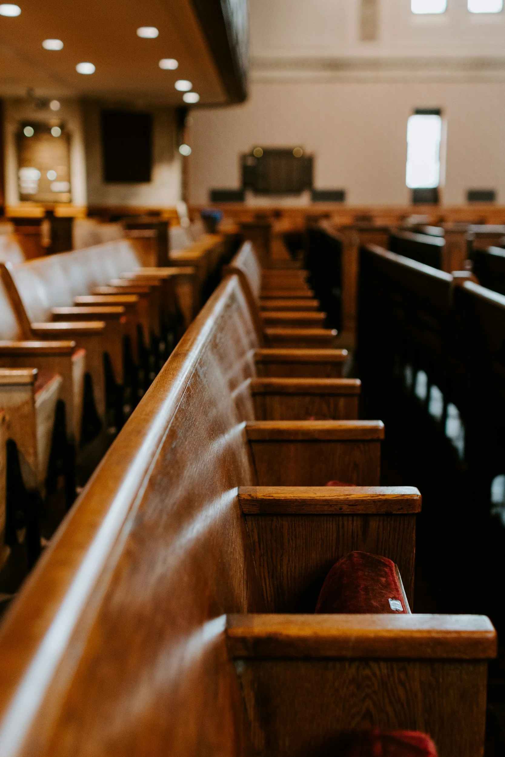 Empty wooden church pews inside a chapel with large windows and soft natural lighting.