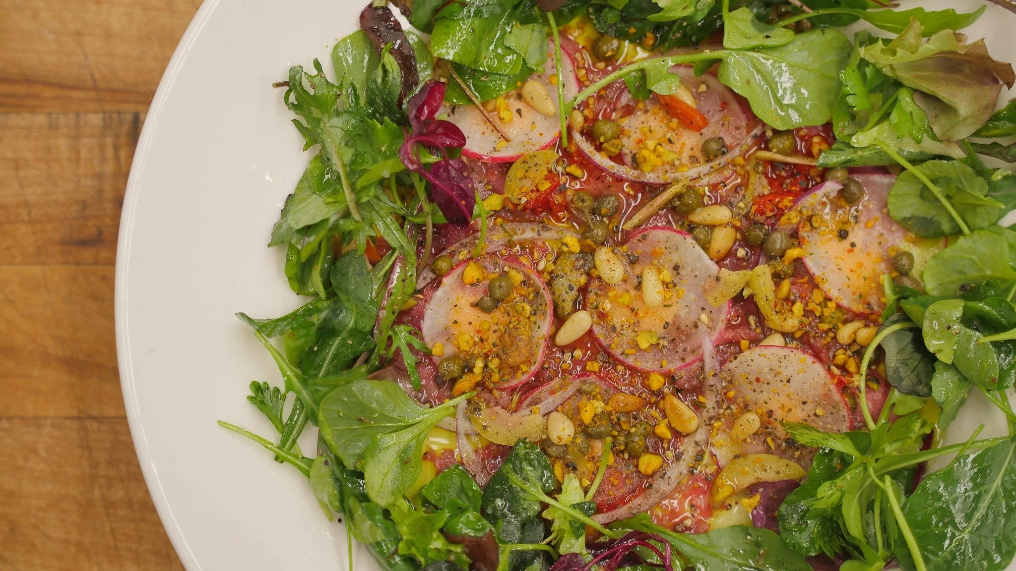 Mixed green salad with radish slices, pine nuts, and a vinaigrette dressing on a white plate