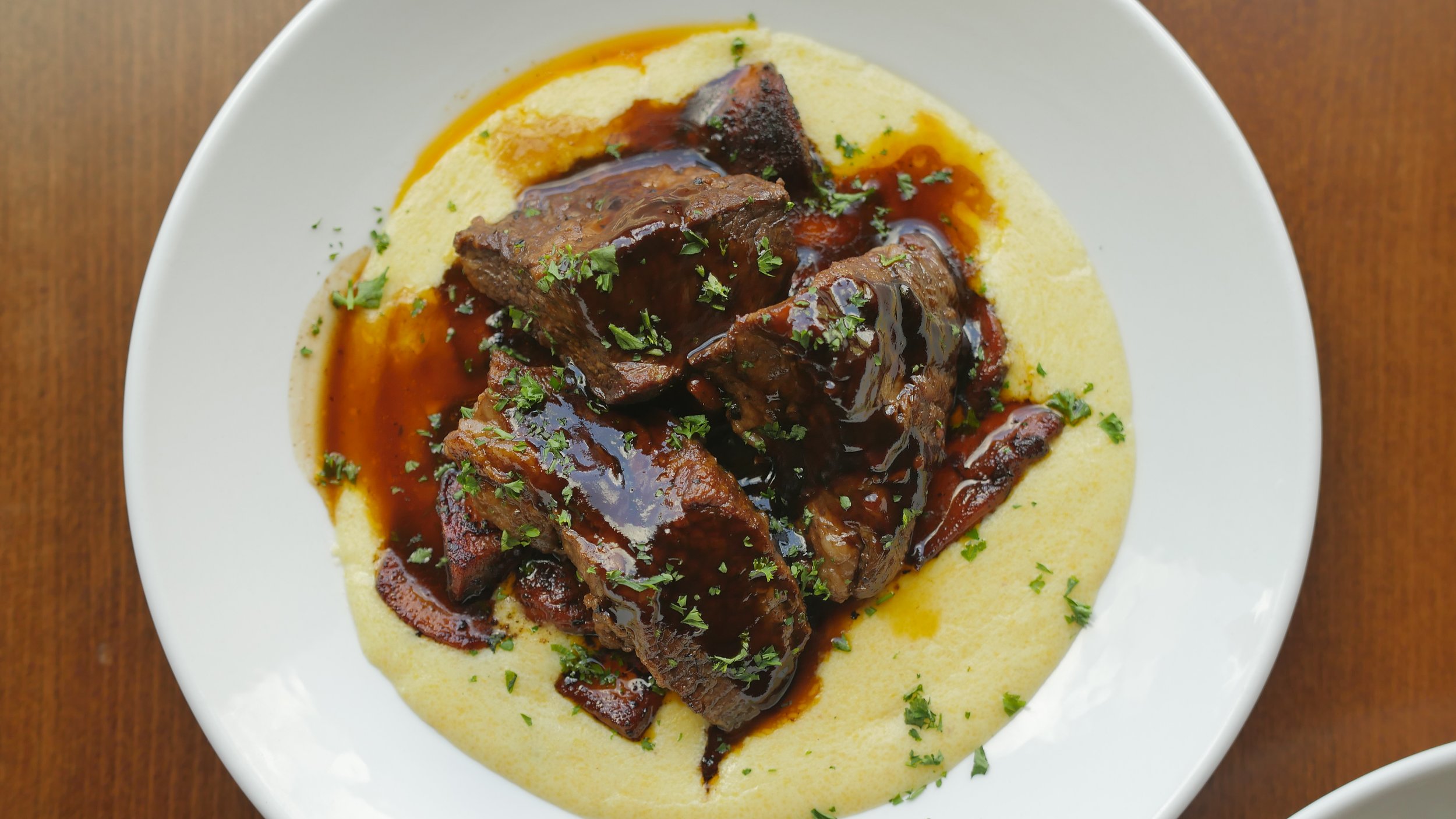 Beef stew with carrots and herbs over mashed potatoes on a white plate.