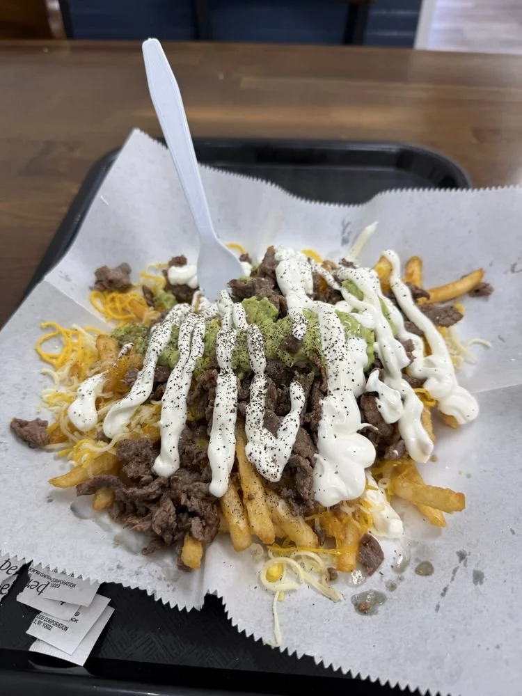 A tray of loaded French fries topped with ground beef, shredded cheddar cheese, sour cream, and black pepper, served on parchment paper.
