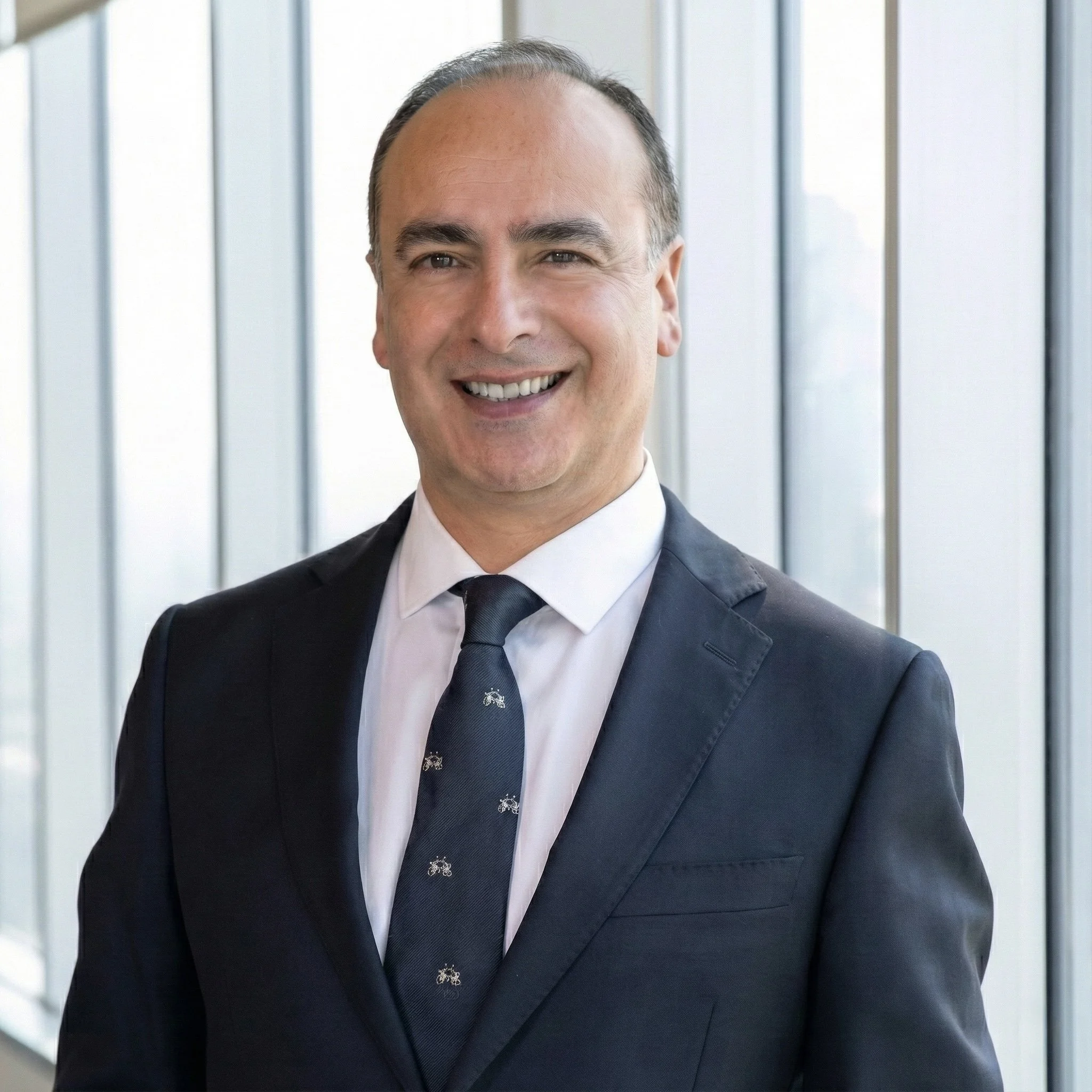 Retrato de un hombre sonriente con traje en un entorno de oficina moderna.