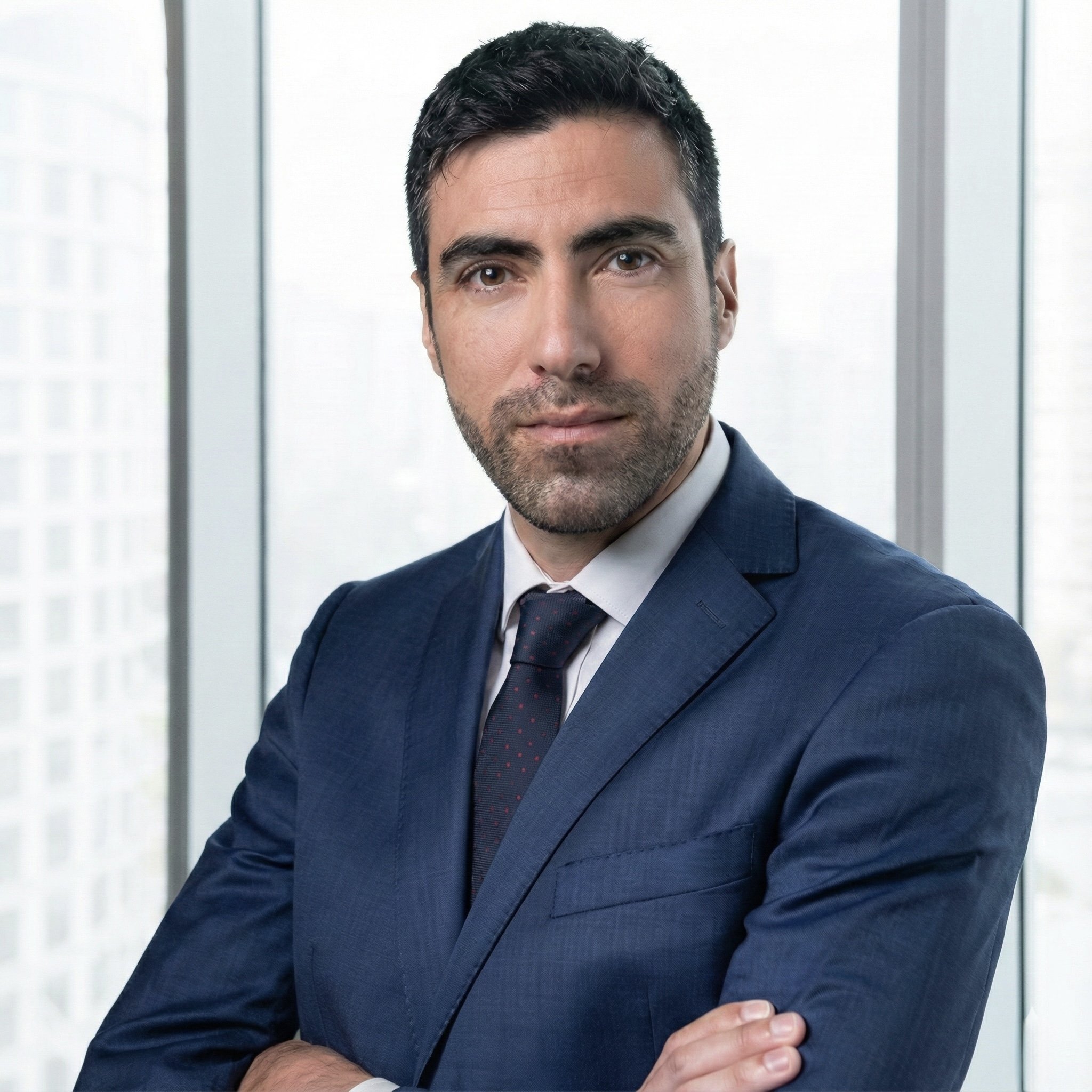 Hombre con traje azul y corbata en oficina moderna con ventanas de ciudad al fondo.