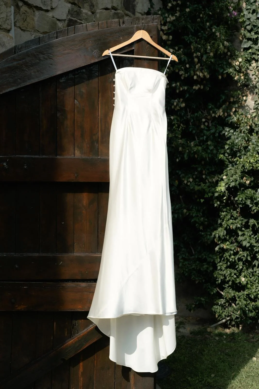 A white wedding dress by Thuy Nguyen Couture hanging on a wooden hanger outdoors, with greenery in the background. Bespoke Bridal Brisbane.