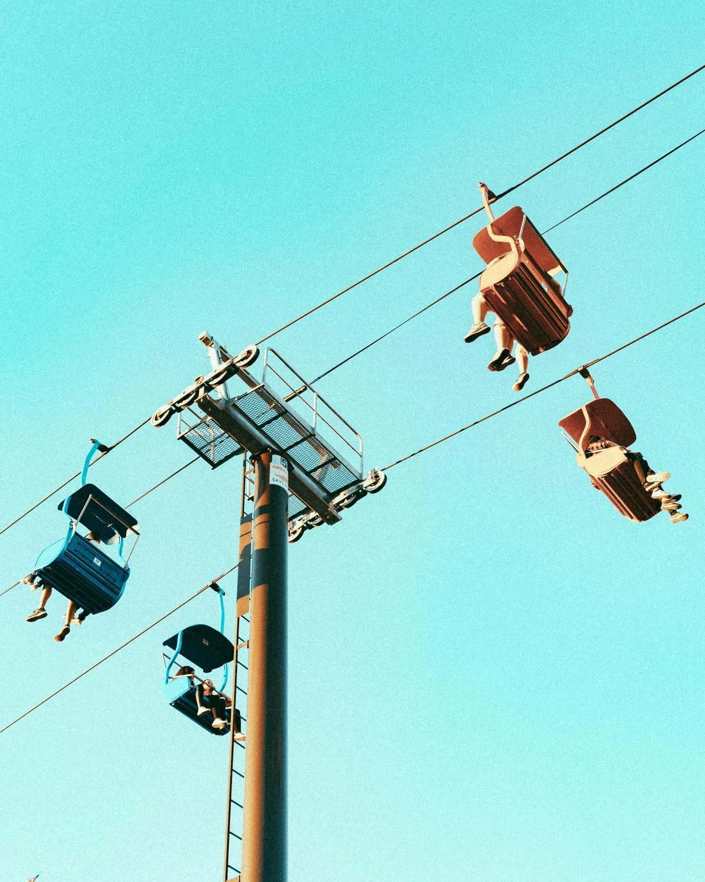 State Fair North Carolina Sky Gazer: People riding on colorful amusement park swings suspended from a cable against a clear blue sky.