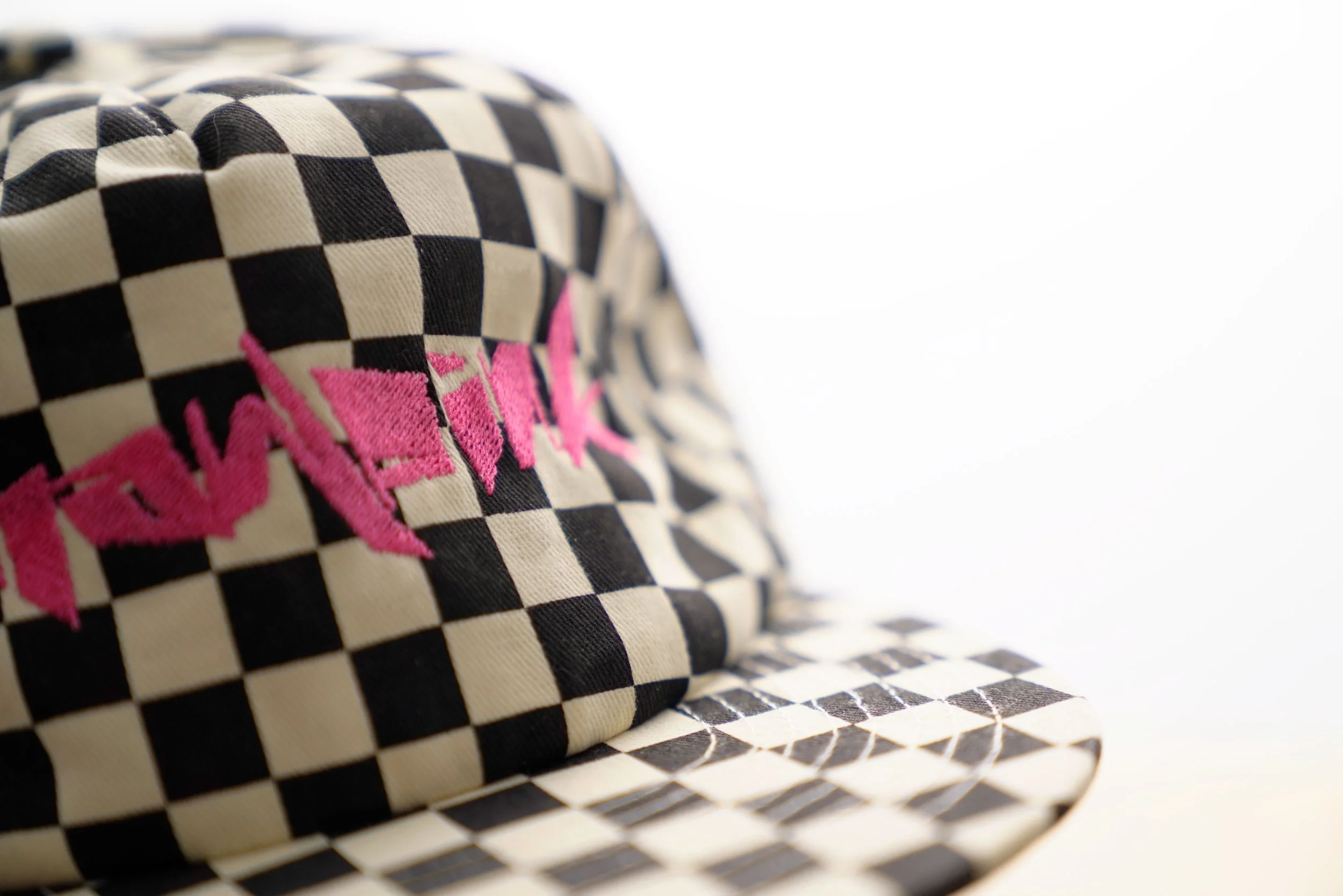Close-up of a black and white checkered hat with pink embroidered text.