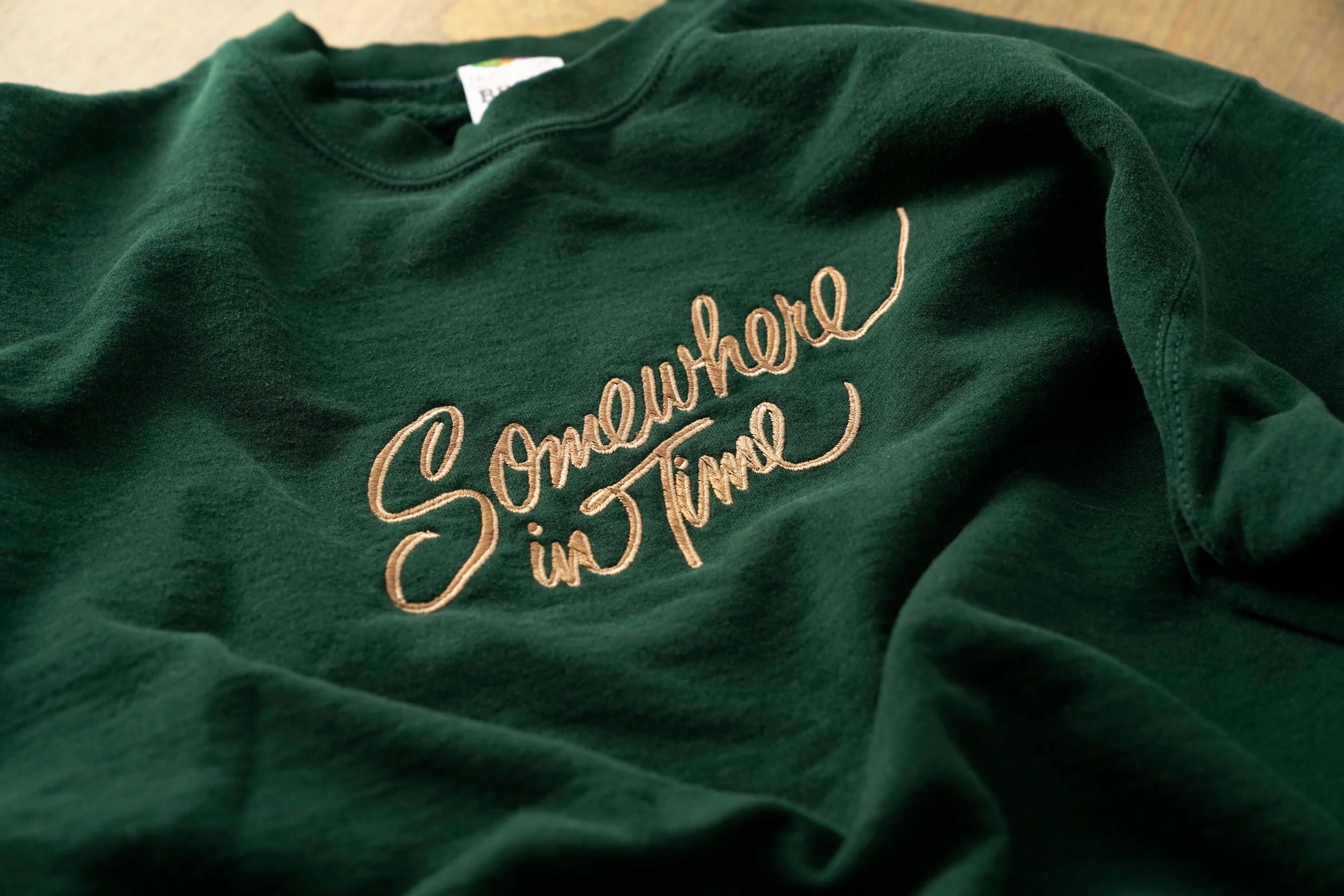 A green sweatshirt with embroidered text that says "Somewhere in time."