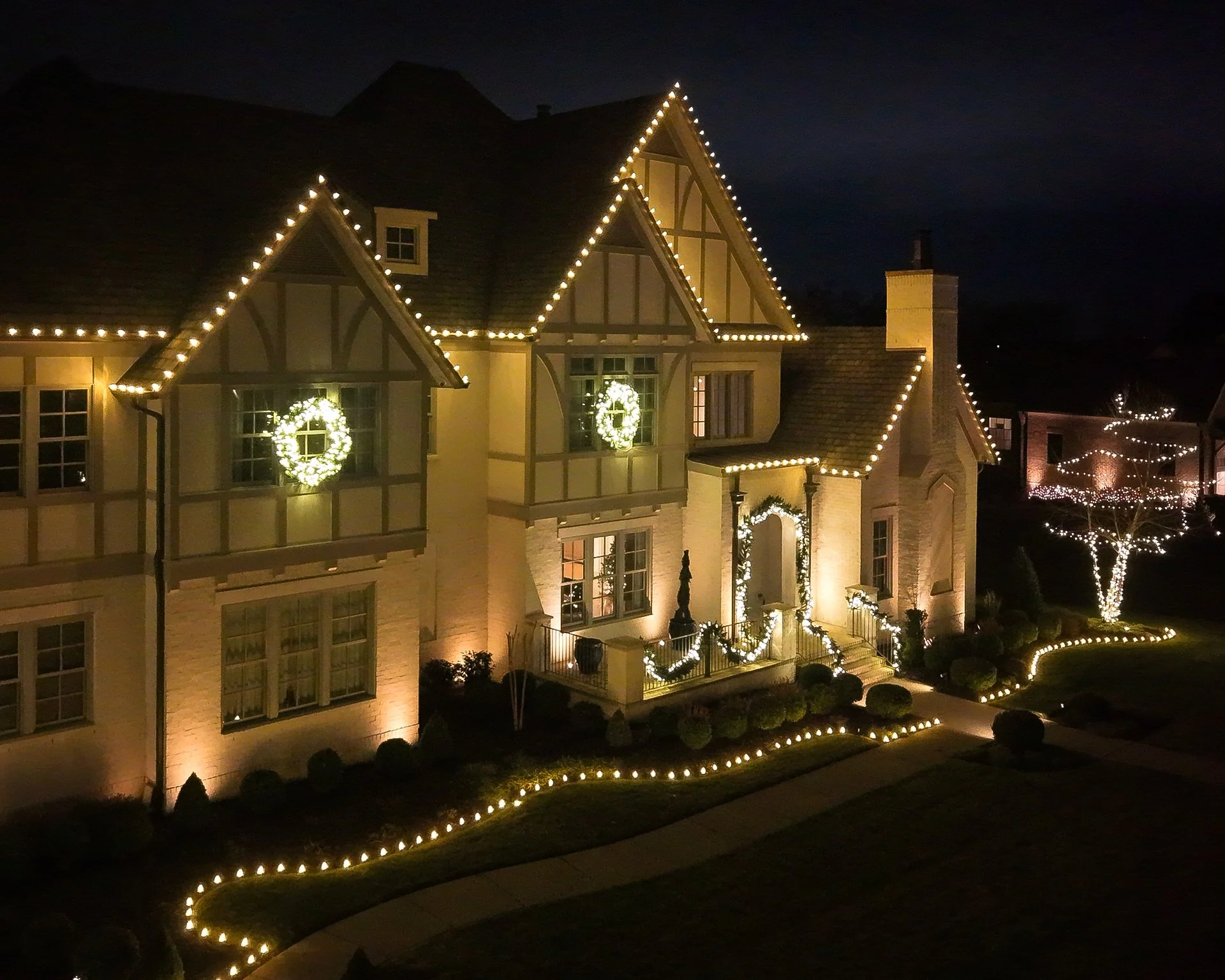 A large house decorated with Christmas lights and wreaths at night.